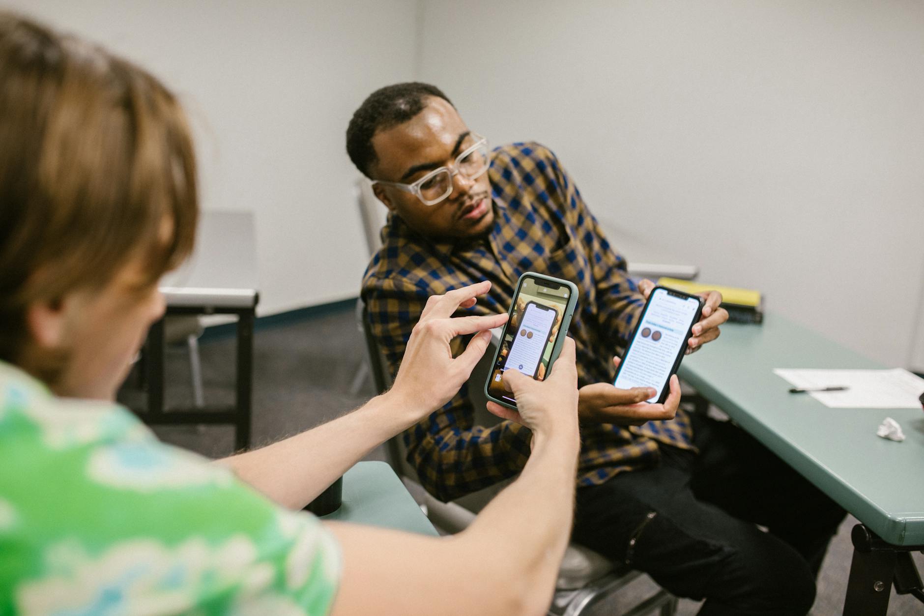 Two students collaborate, exchanging information on smartphones during a classroom session.