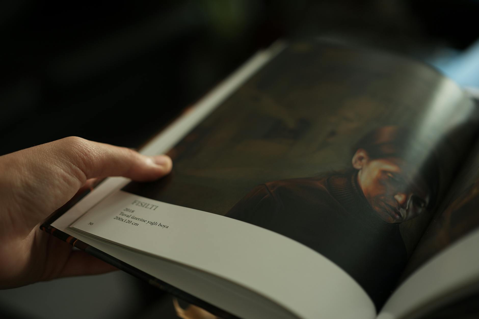 Hand holding a book displaying an artistic portrait of a person on a page.