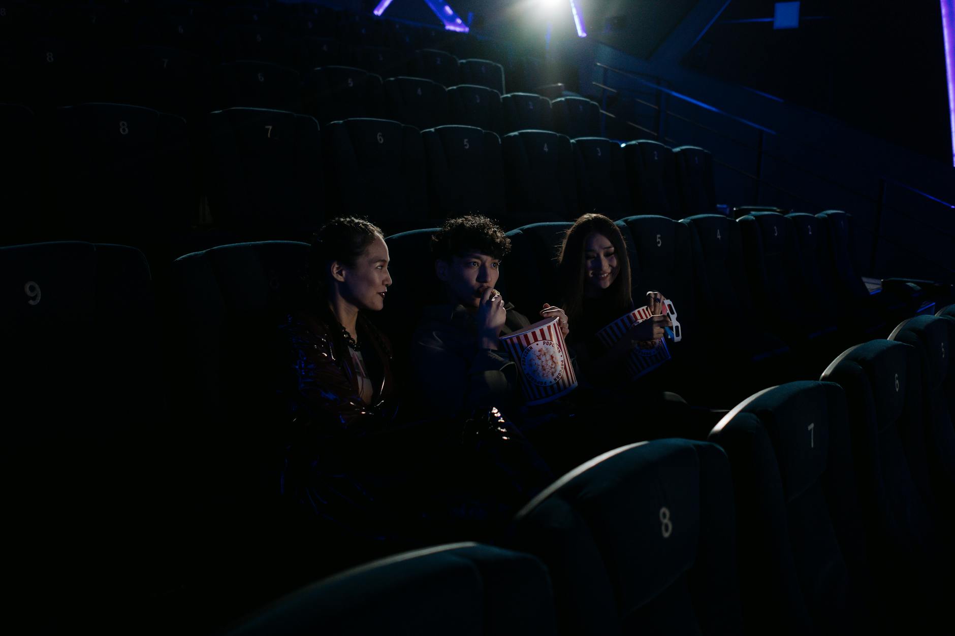 Group of friends watching a movie at a cinema while enjoying popcorn.