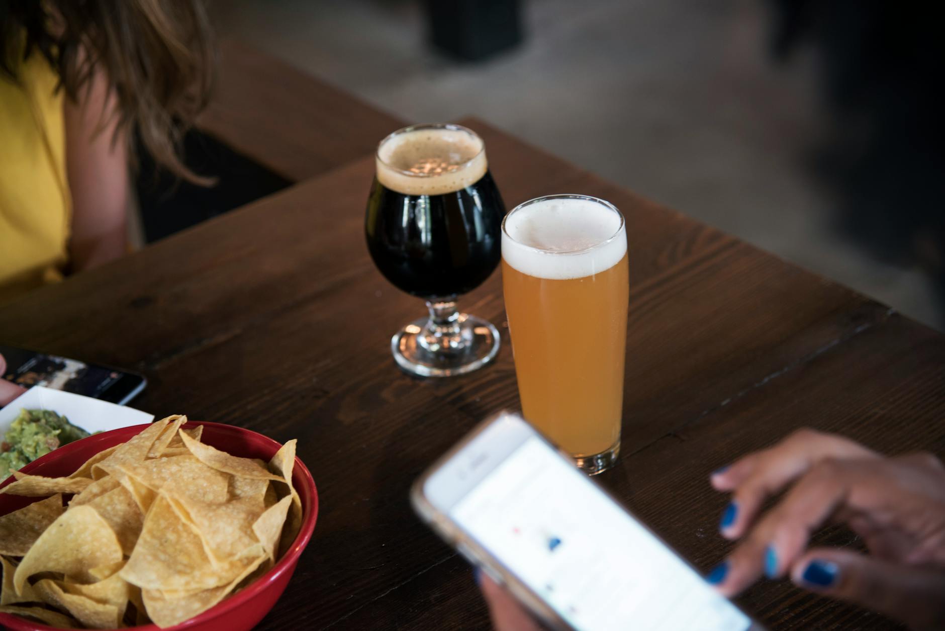 Two types of craft beer and snacks at a bar with people socializing.