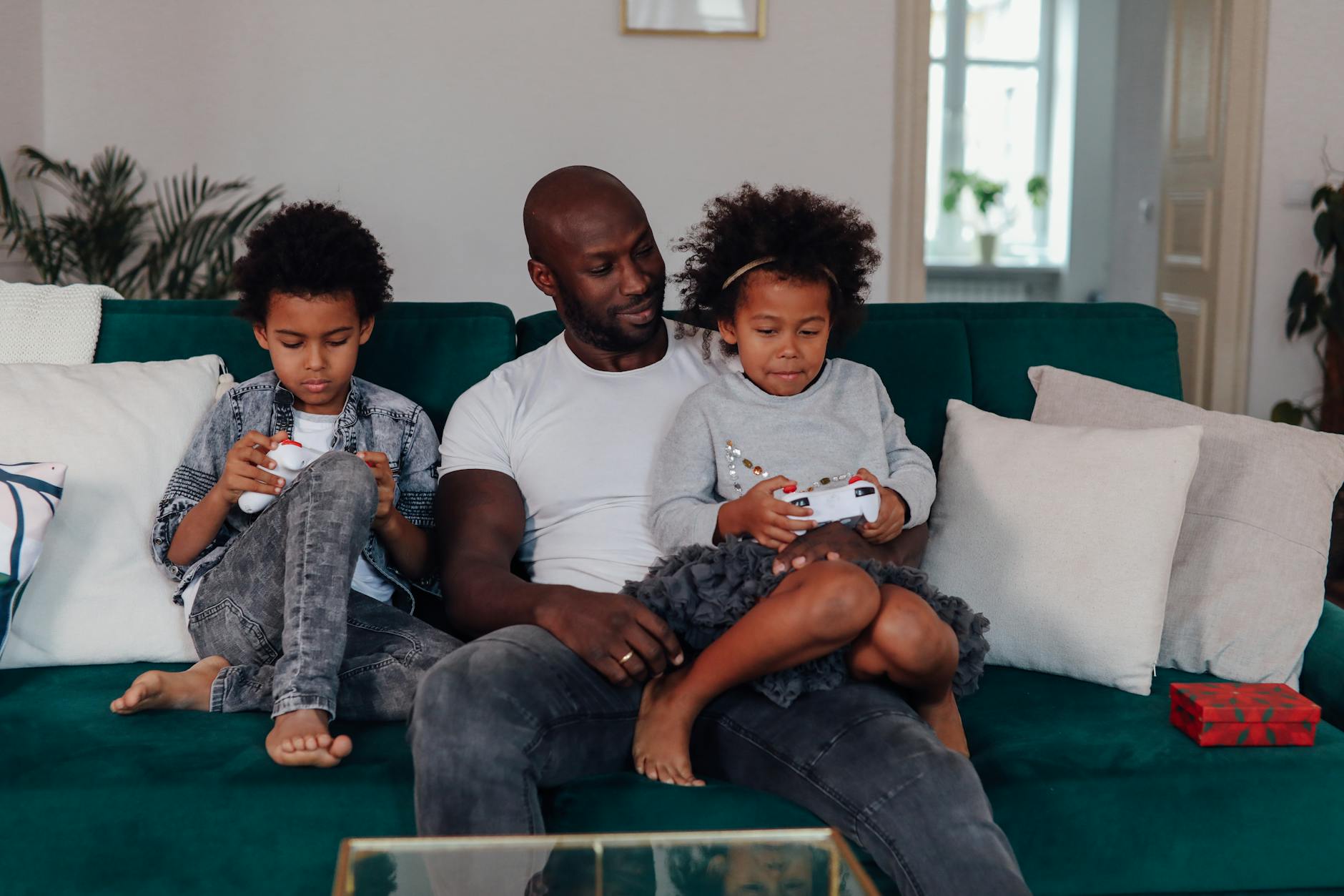 A father and his two children enjoy playing video games together indoors, promoting family togetherness.