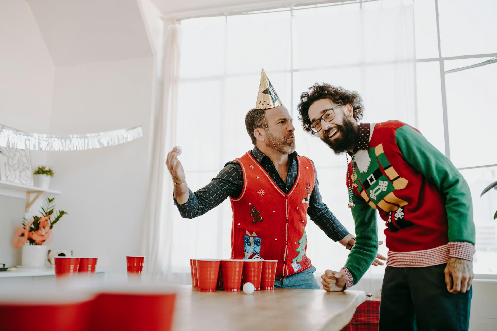 Two adults enjoying a Christmas-themed office party with beer pong and festive sweaters.