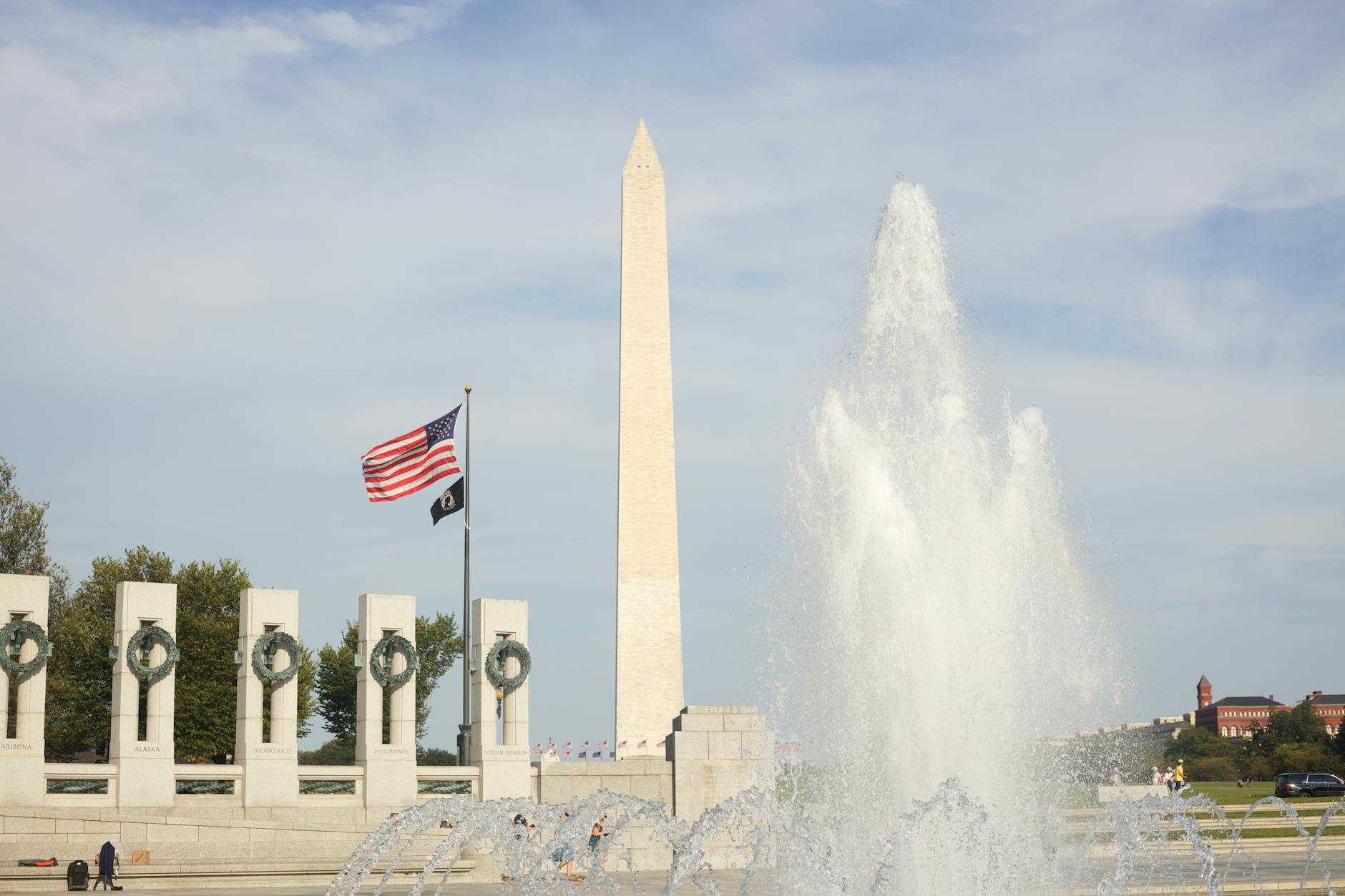 Iconic Washington Monument with a vibrant fountain and American flags under a clear blue sky.