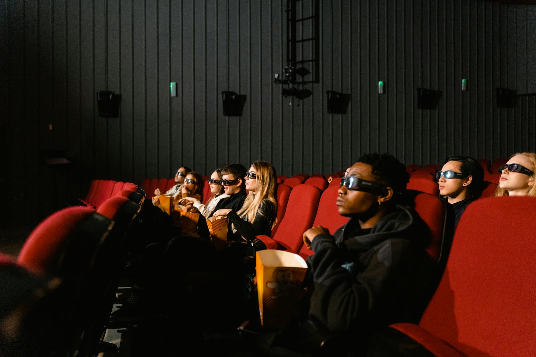 People enjoying a movie night with 3D glasses in a cinema, eating popcorn.