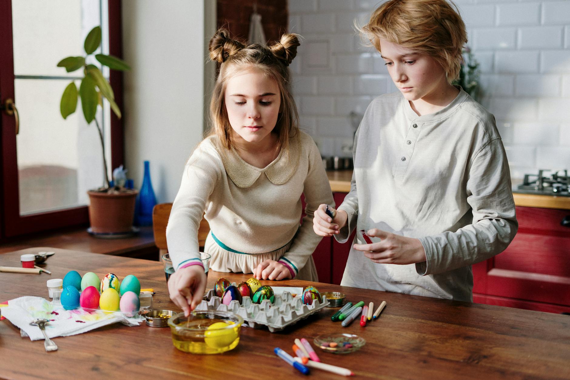 Kids engaged in Easter egg decoration with paints in a cozy kitchen setting.