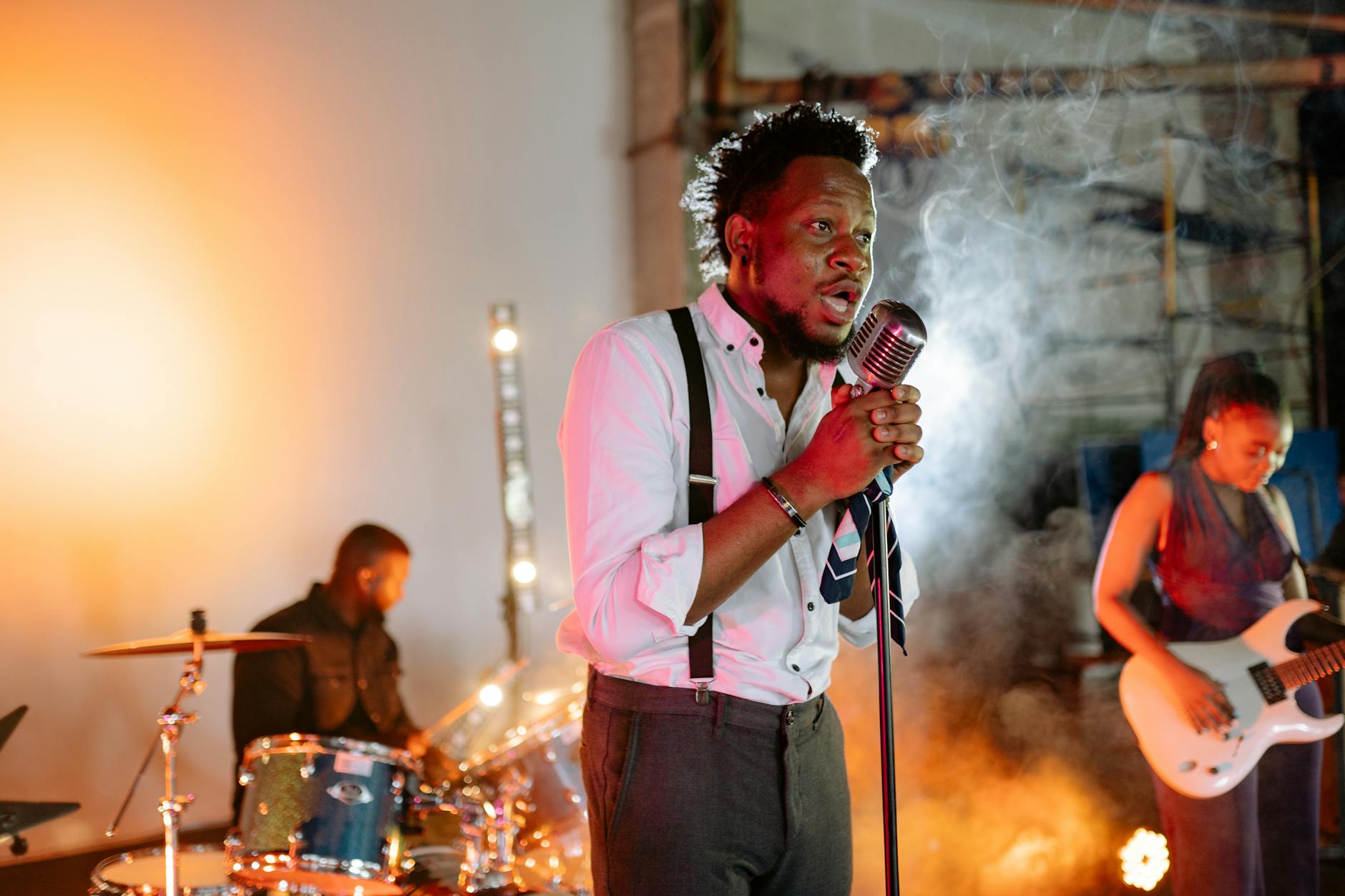 A vibrant indoor band performance featuring a singer, drummer, and guitarist in action.