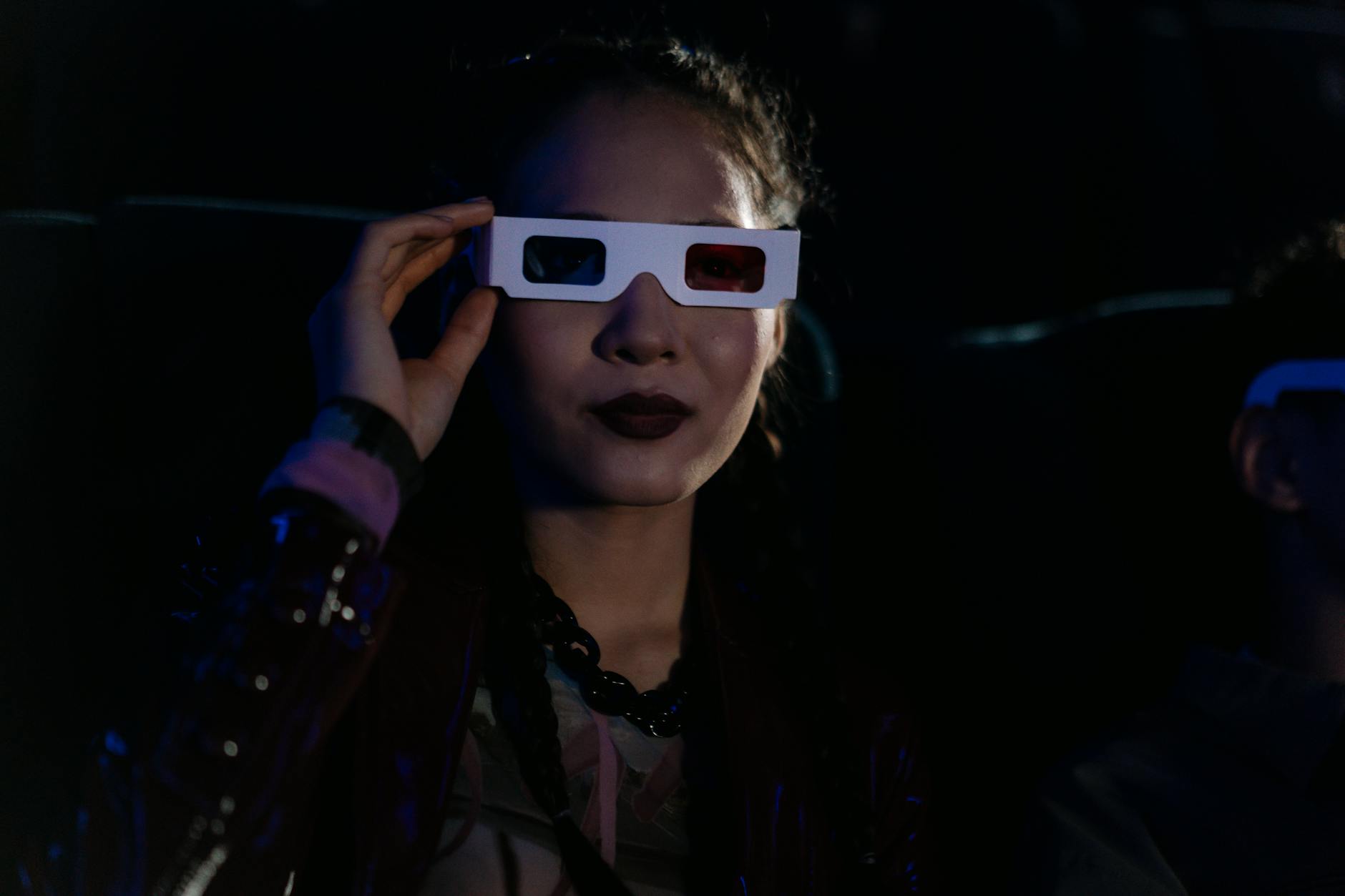 A woman in a dark cinema wearing 3D glasses, enjoying an immersive movie experience.