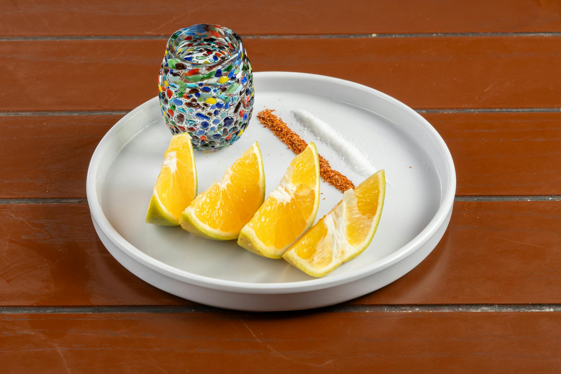 Vibrant mosaic glass with citrus wedges on a plate, styled elegantly for an artistic shot.