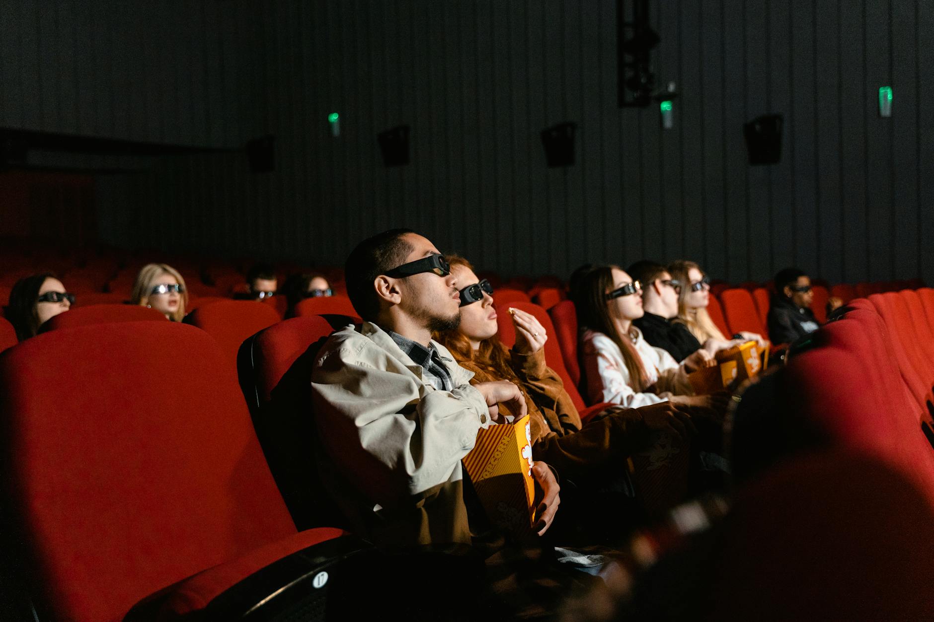 People watching a 3D movie in a theater, with popcorn in hand, fully immersed.