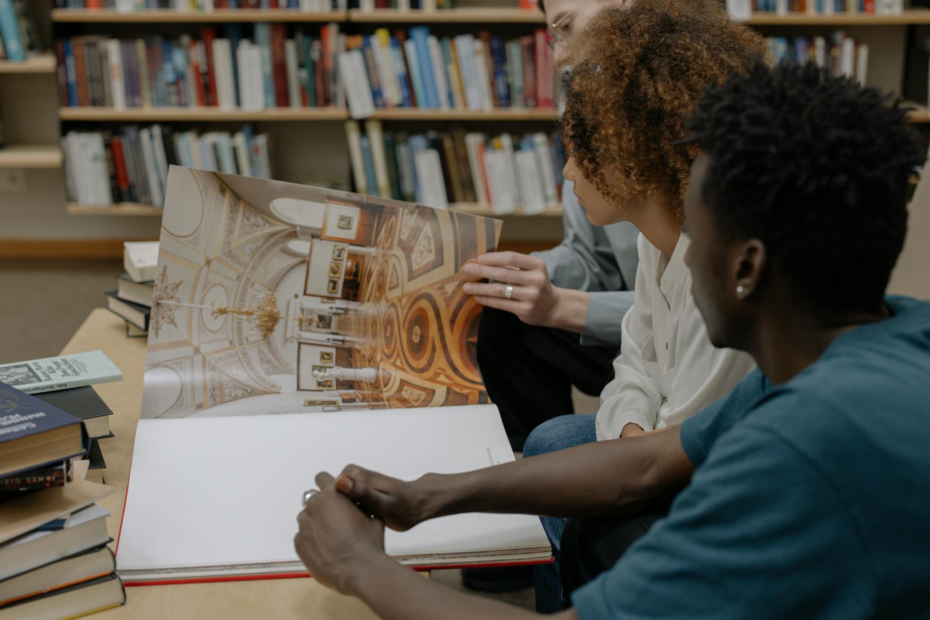 A diverse group of adults studying a large book together in a library setting.