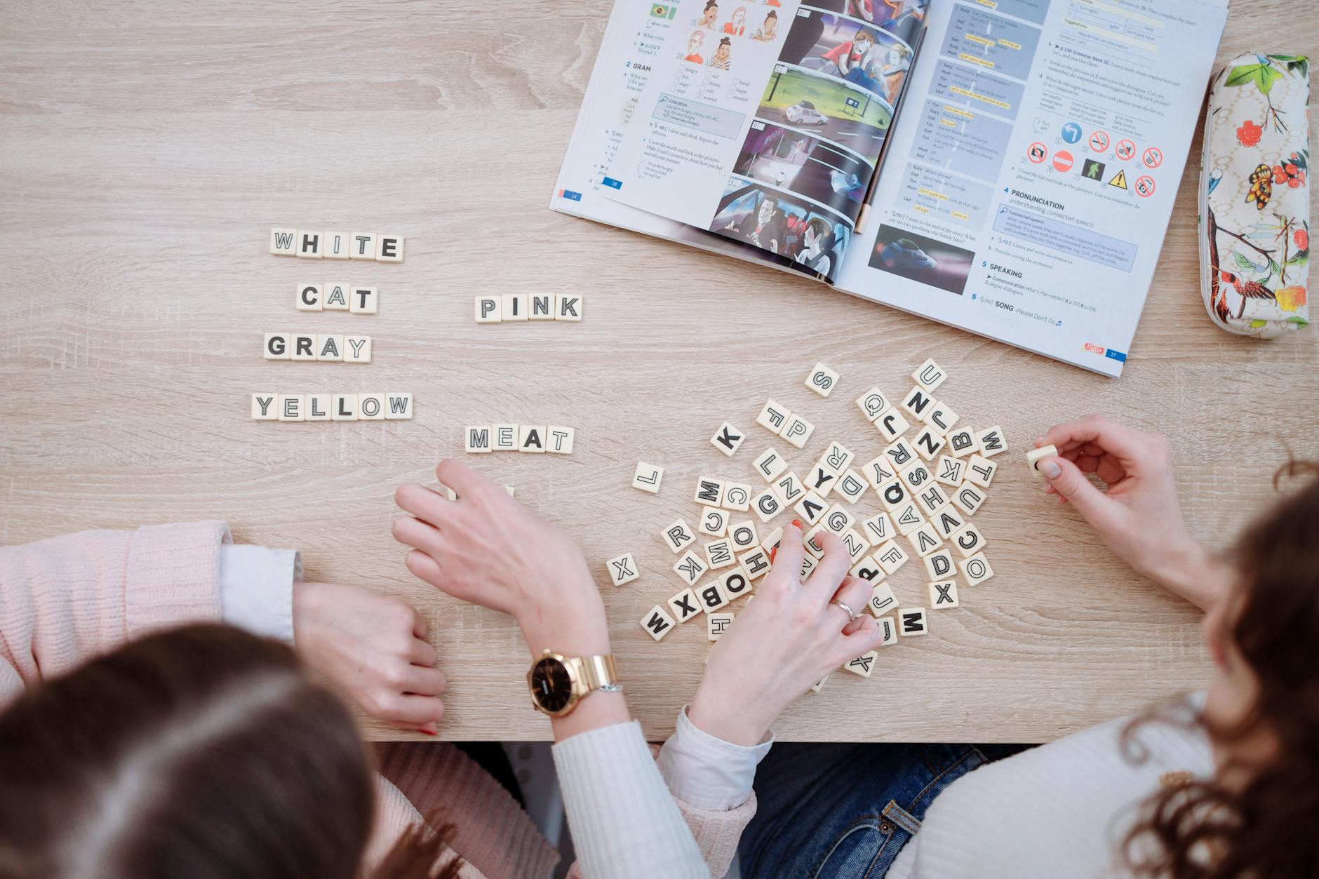 Friends studying together using Scrabble tiles and books, fostering collaborative learning in a casual setting.