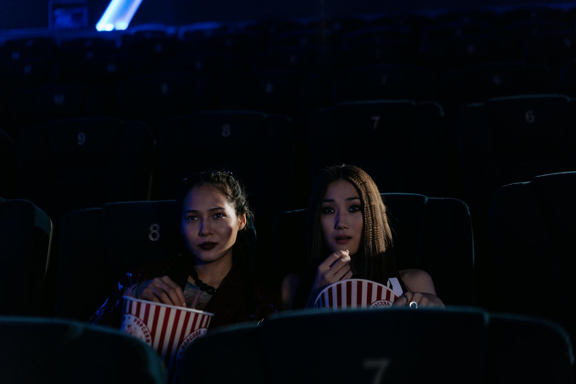Two women sitting in a dark cinema, enjoying popcorn and watching a movie.