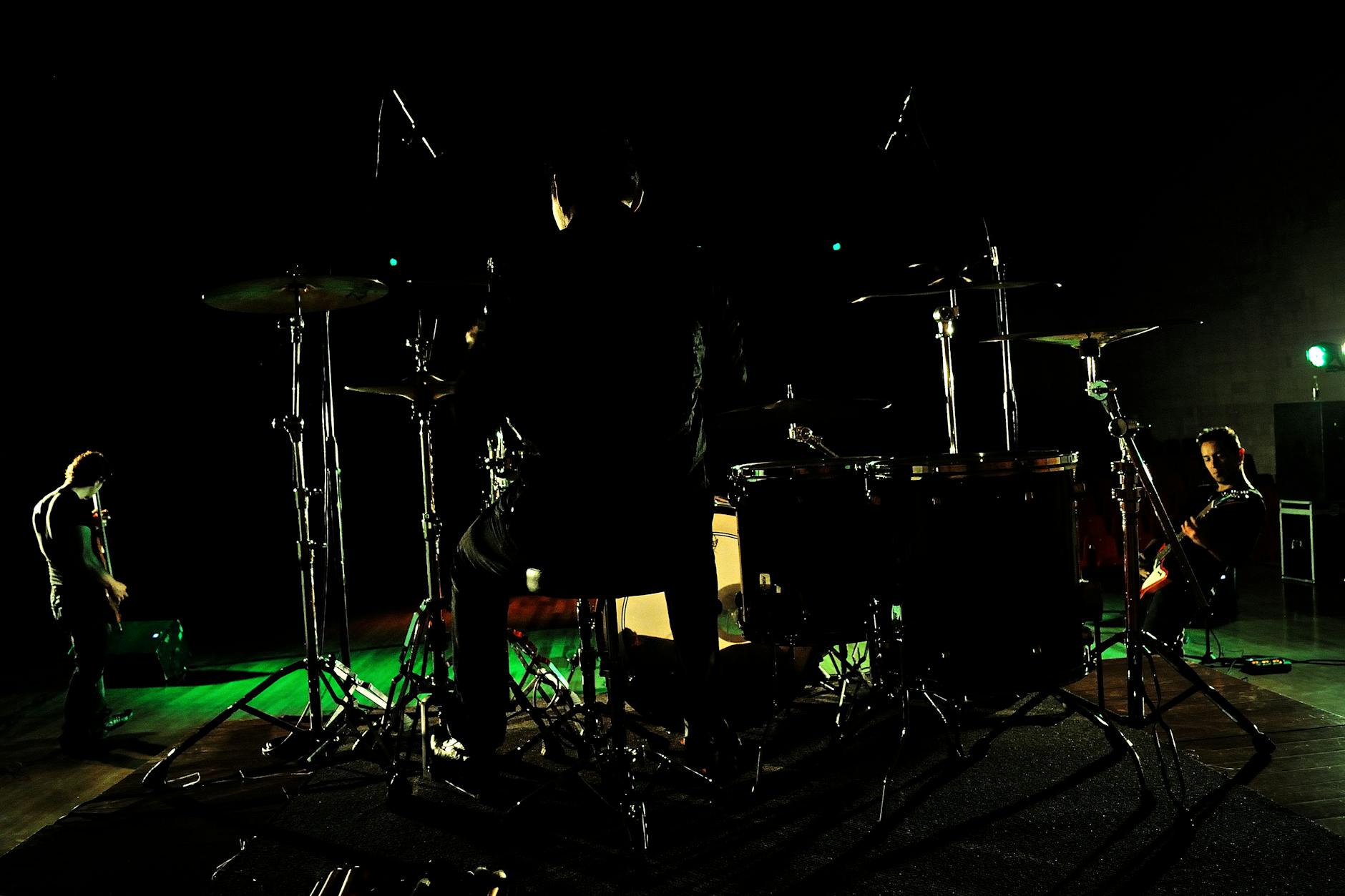 Dynamic stage performance by a rock band with drummer and guitarists under vibrant lights.