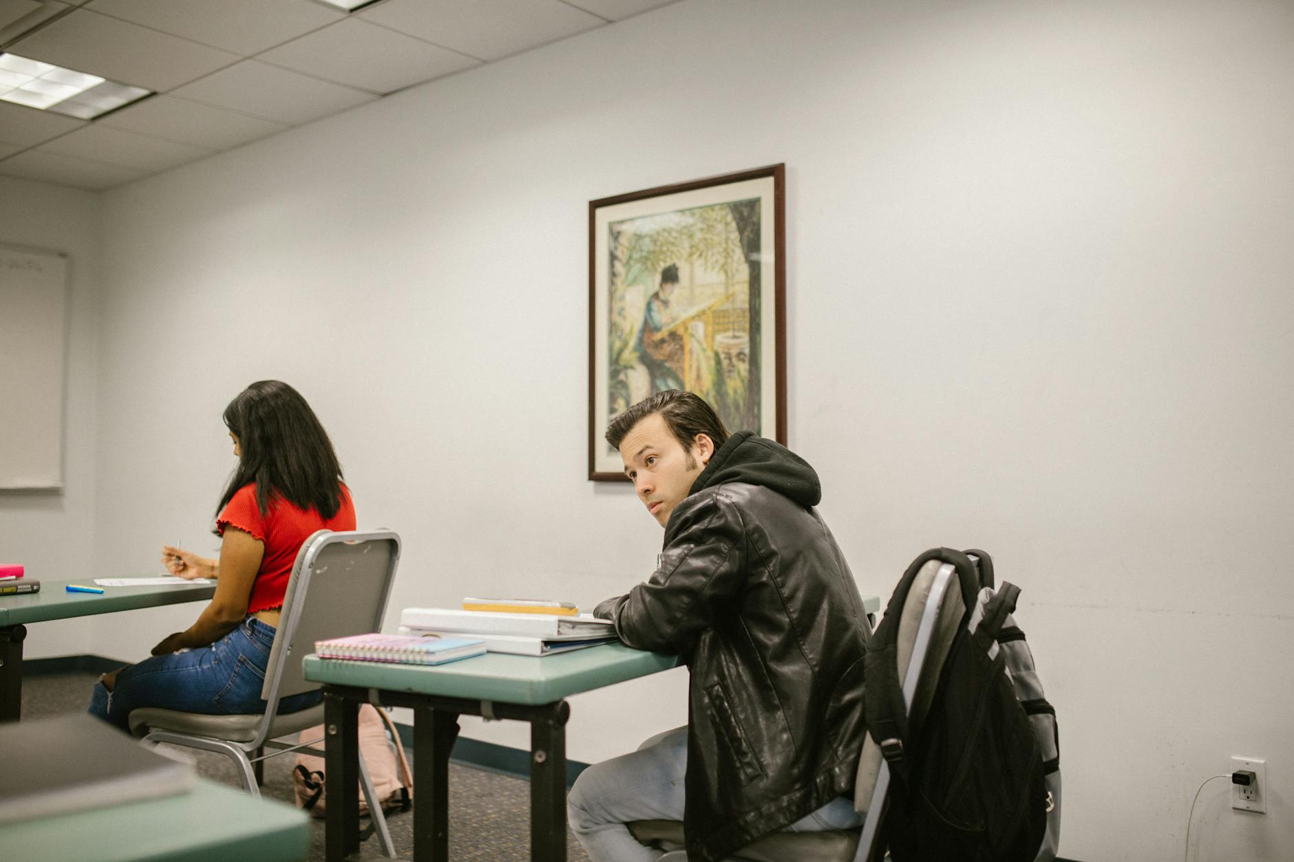 A male and female college students studying in a classroom, focused on their exams.