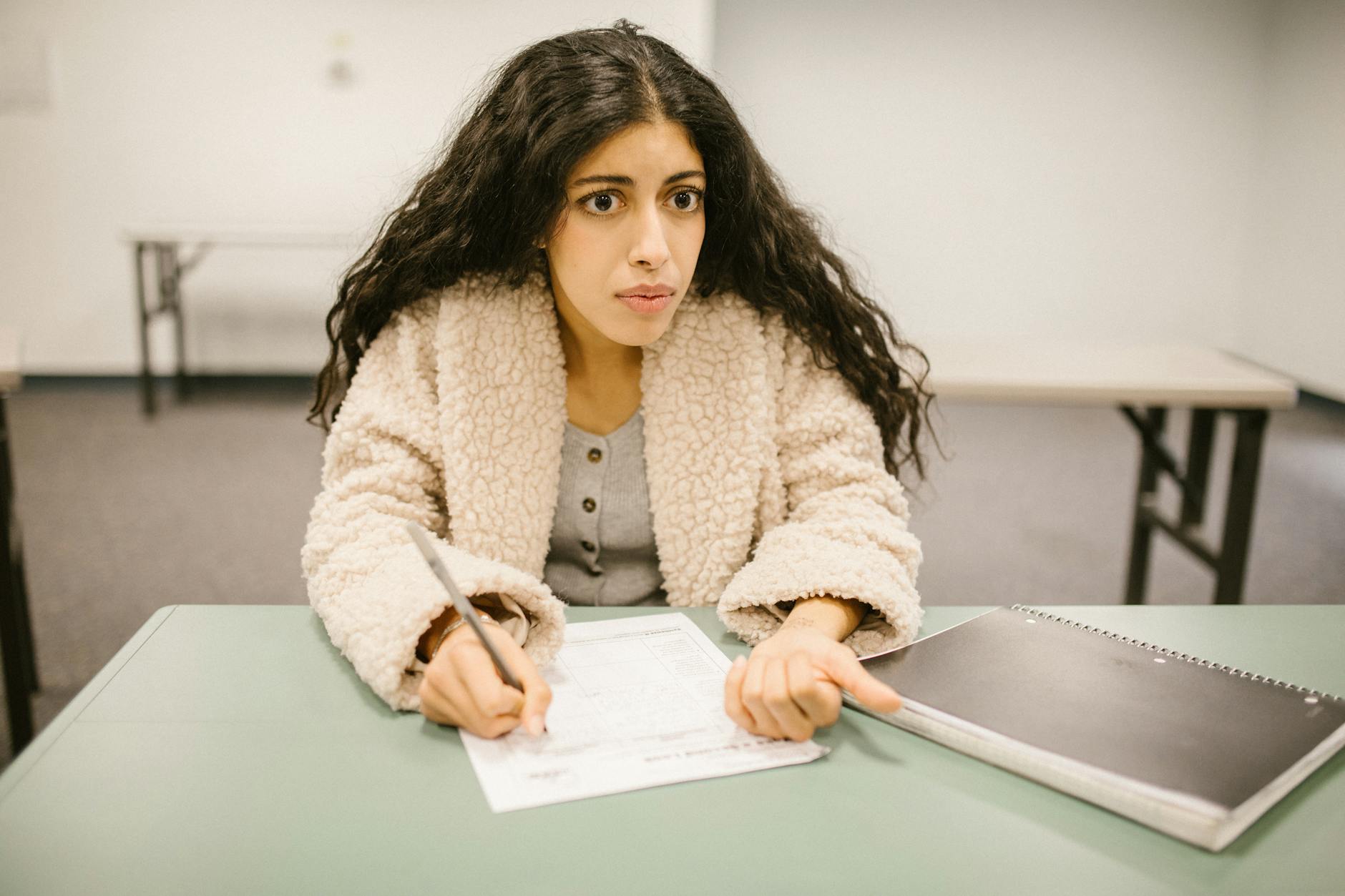 Concentrated woman writing an exam in a classroom setting, showcasing study focus.