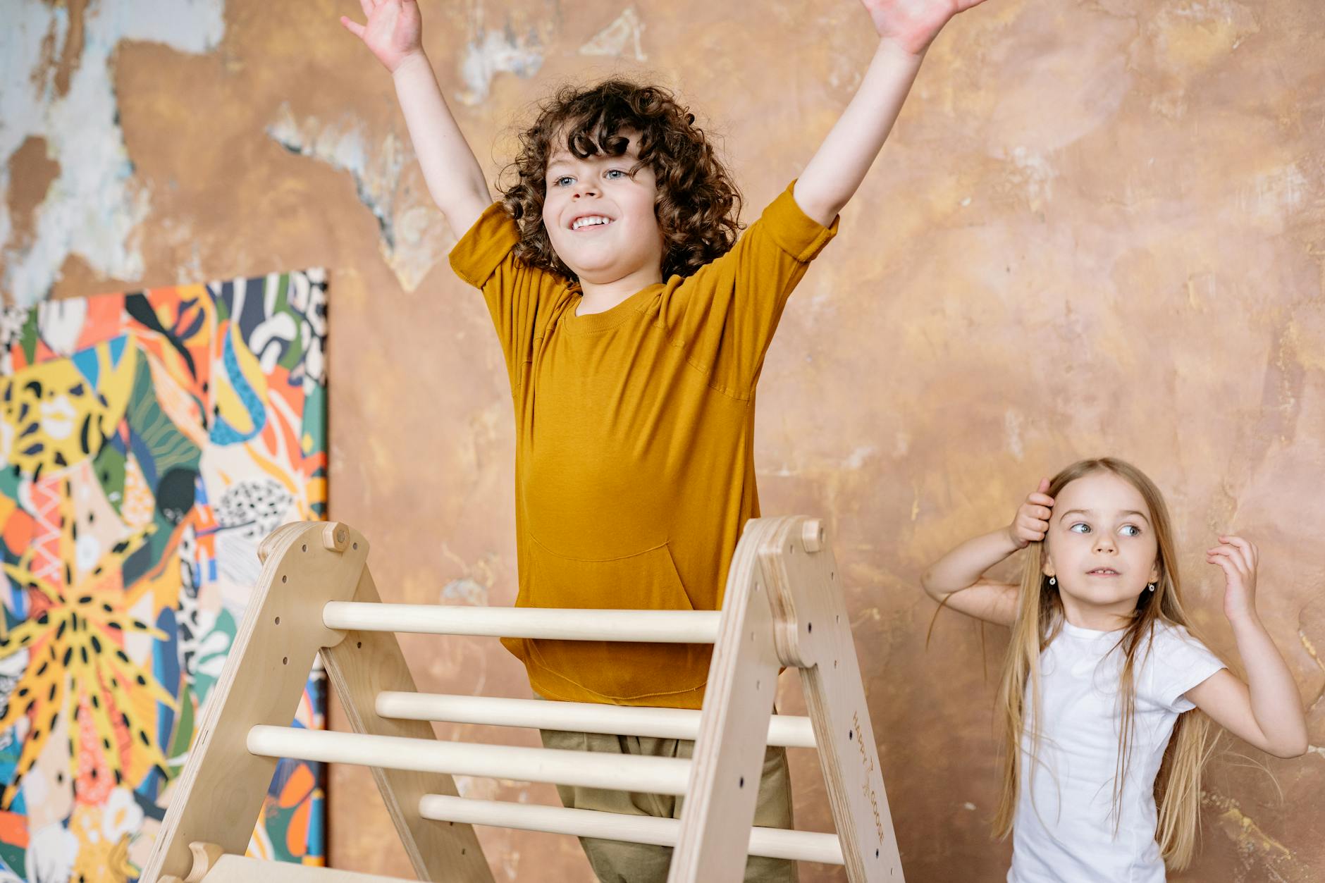 Two cheerful kids playing on a wooden ladder indoors, expressing excitement and fun.