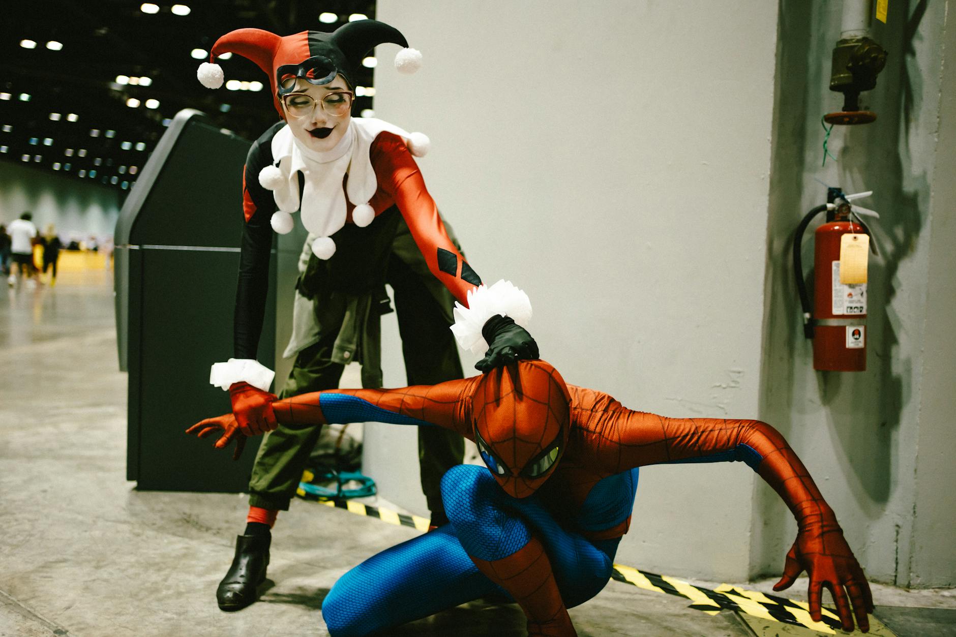 Two cosplayers dressed as Harley Quinn and Spider-Man pose vividly in a convention center.