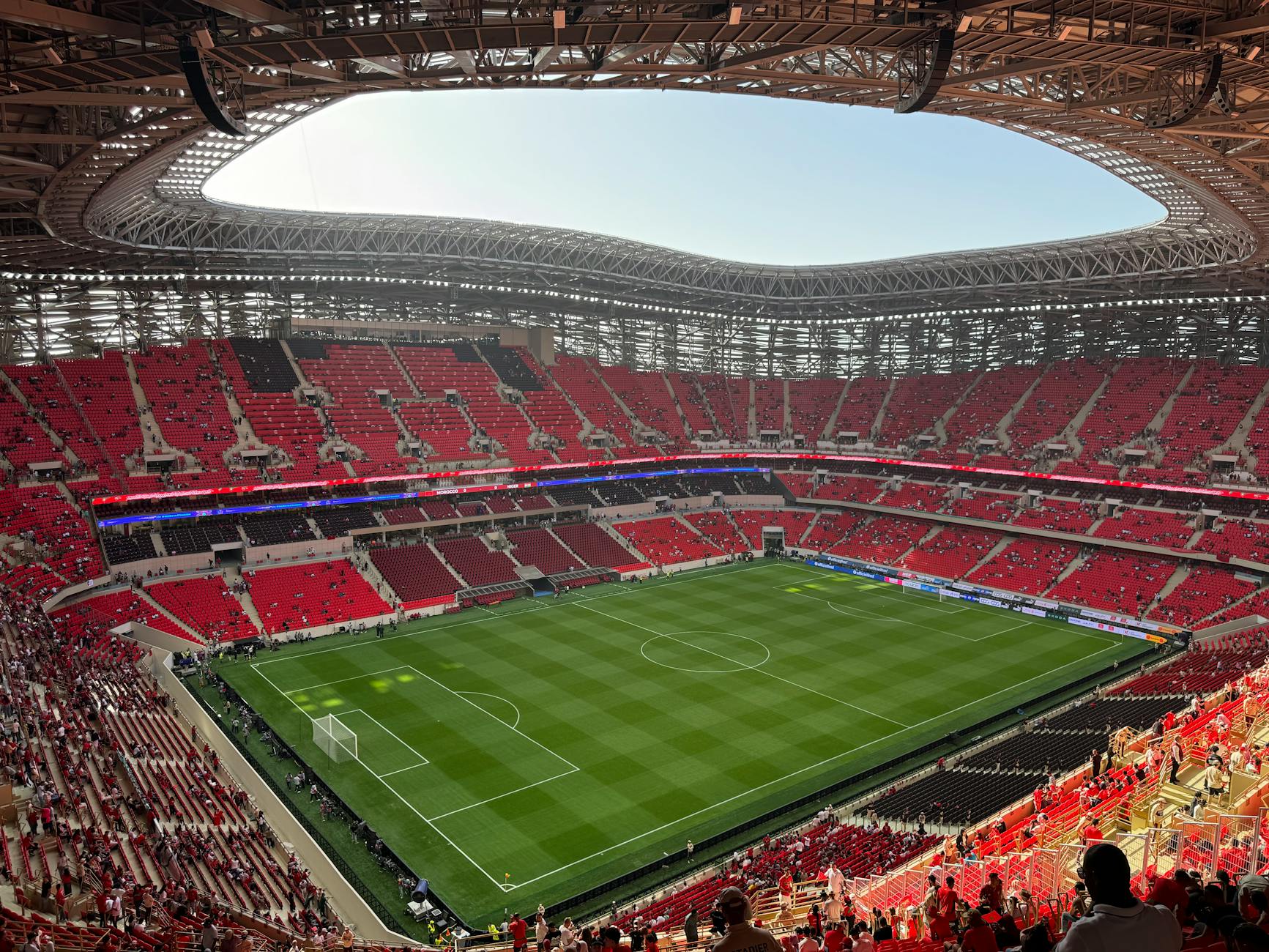 Aerial view of a modern stadium with vibrant red seats and a well-maintained green field.