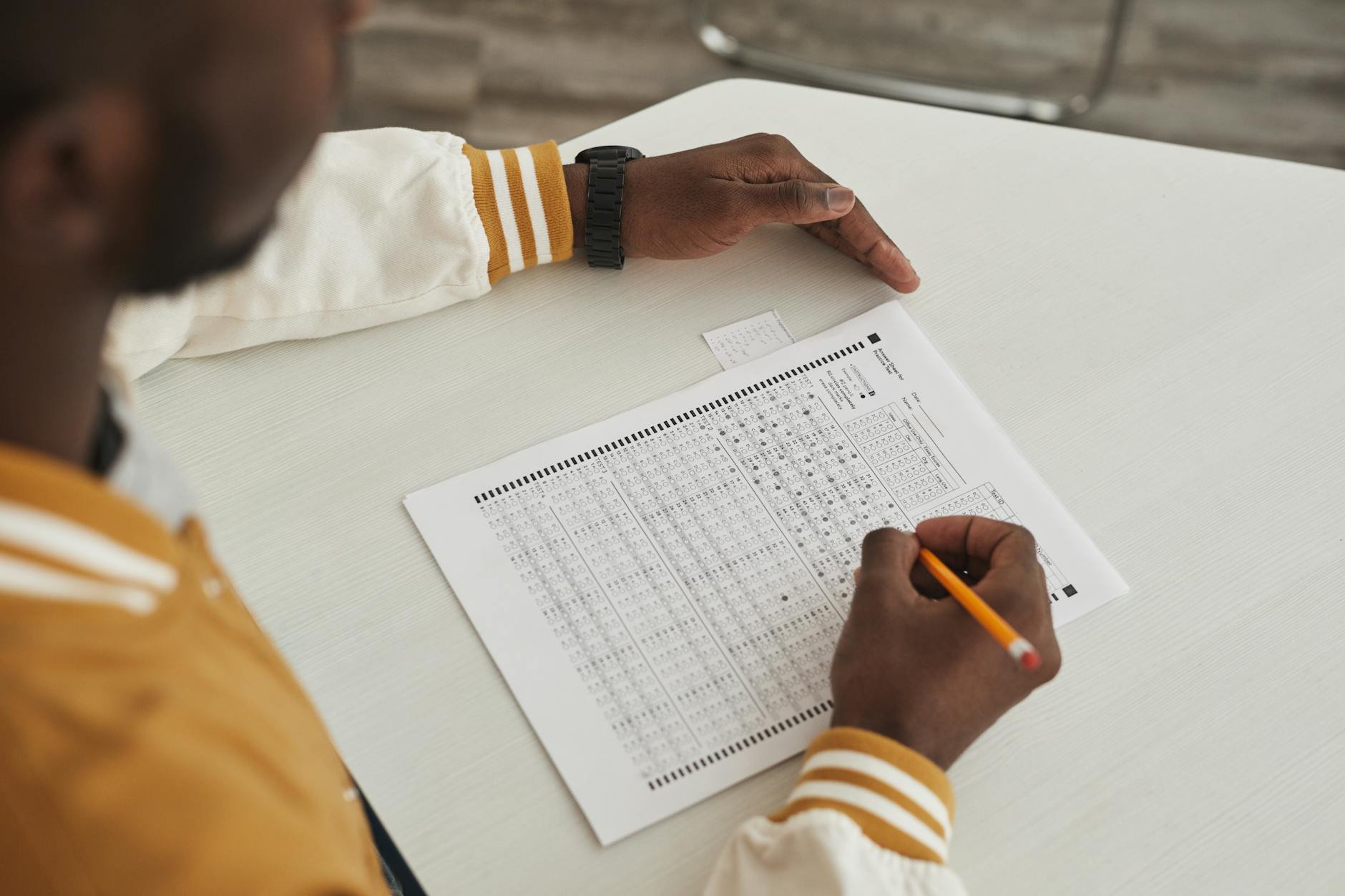 Focused student marking answers on a multiple choice exam sheet in a classroom setting.