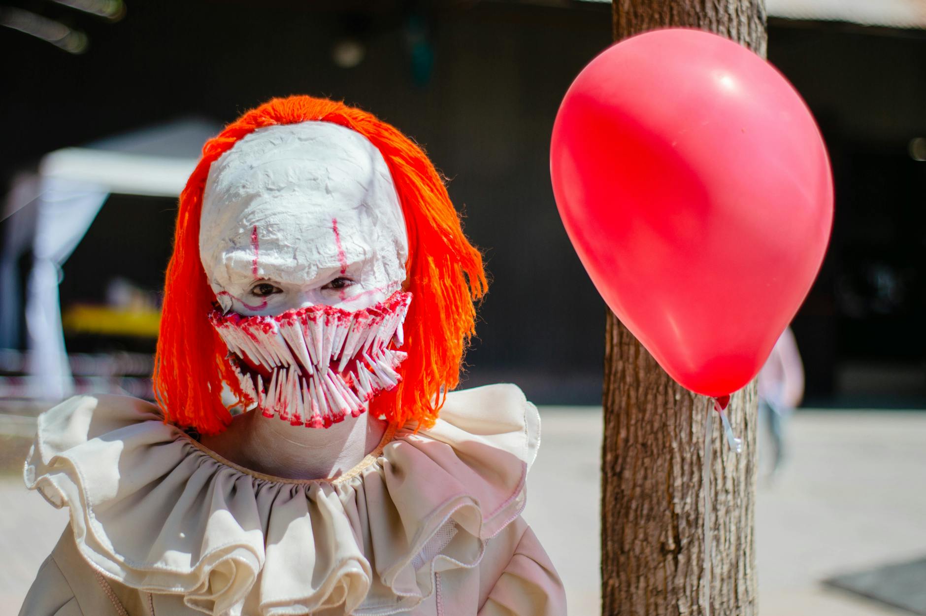 A person in a scary clown costume with a red balloon outdoors, perfect for Halloween themes.