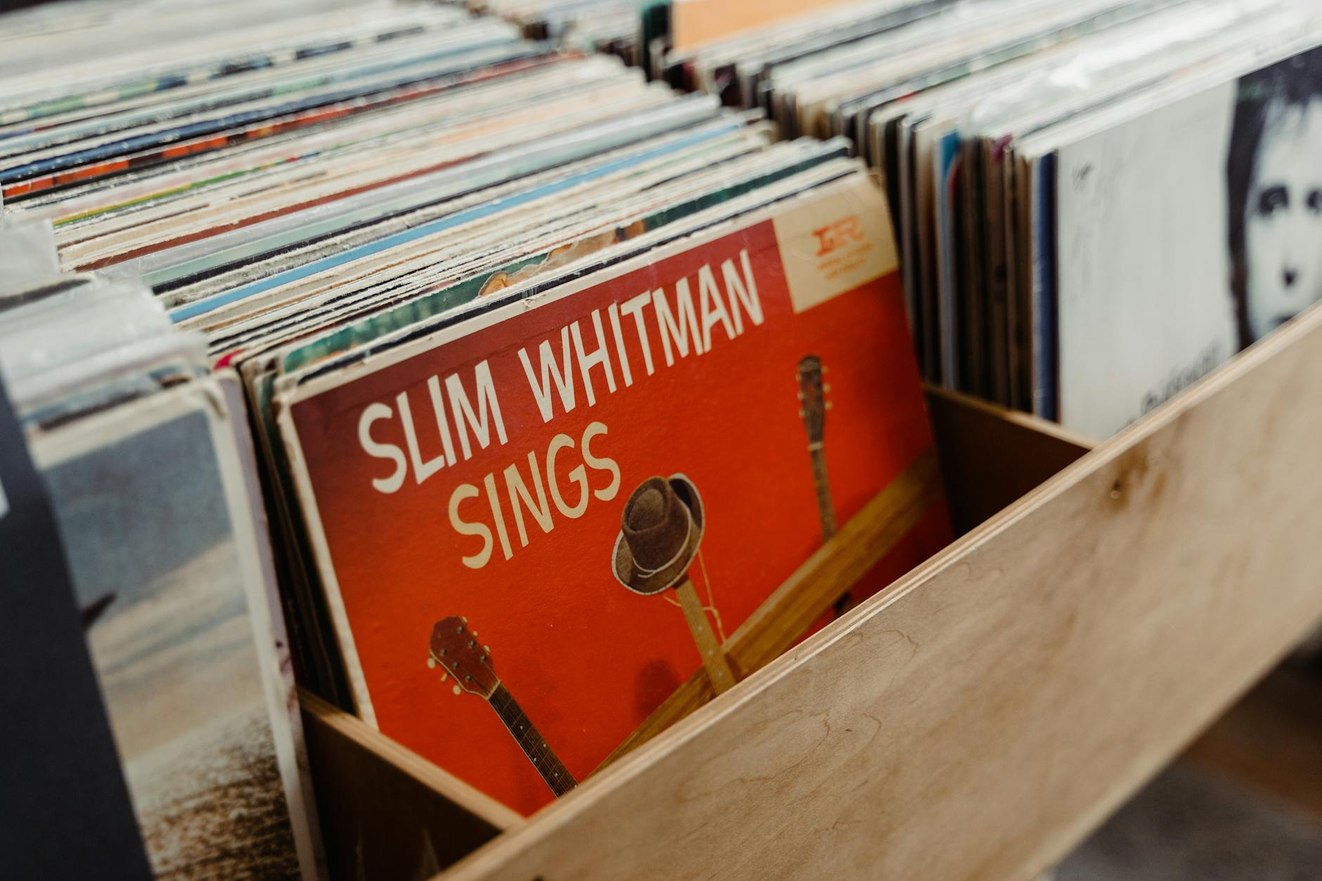 Assorted vinyl records in a wooden crate highlighting 'Slim Whitman Sings' album.