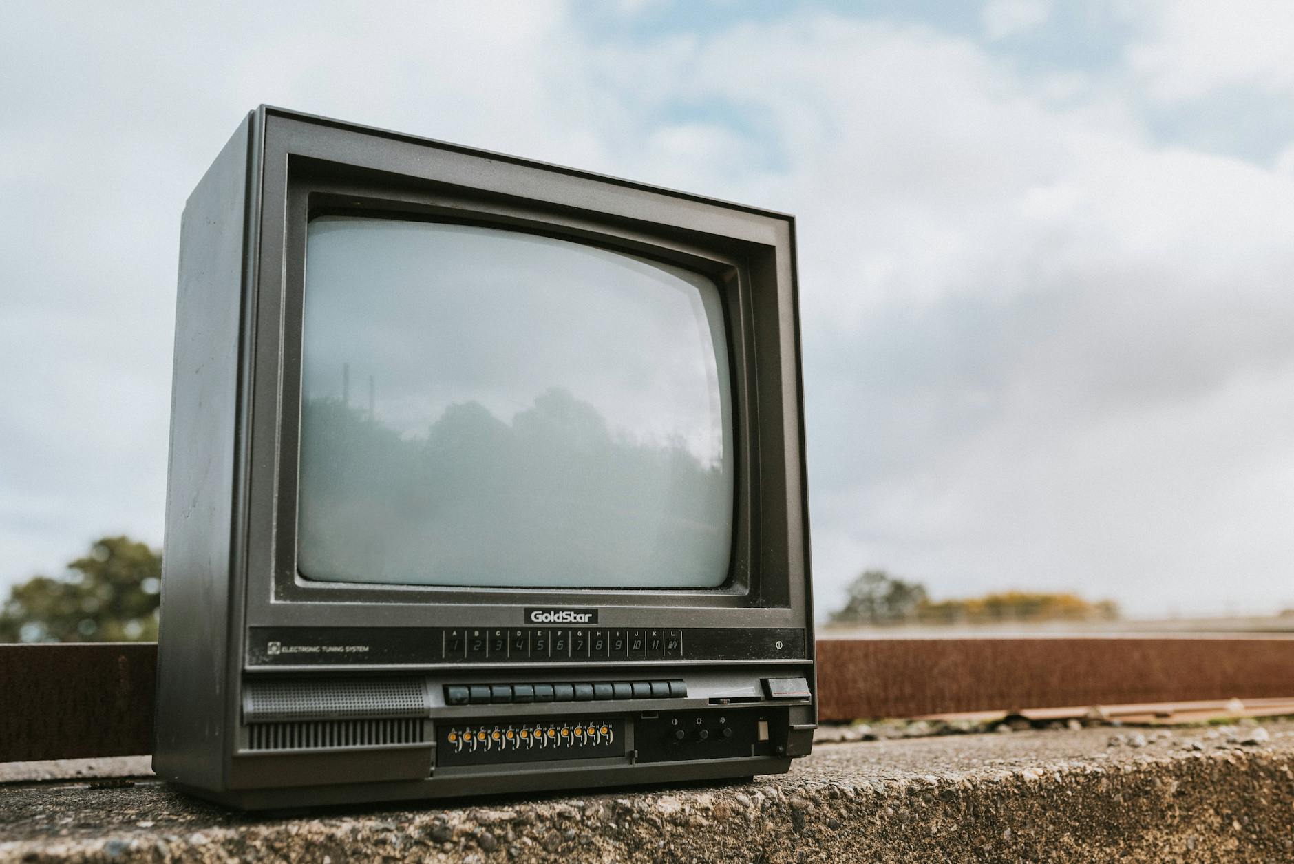 Old CRT television set placed outdoors with a cloudy sky backdrop, evoking nostalgia.