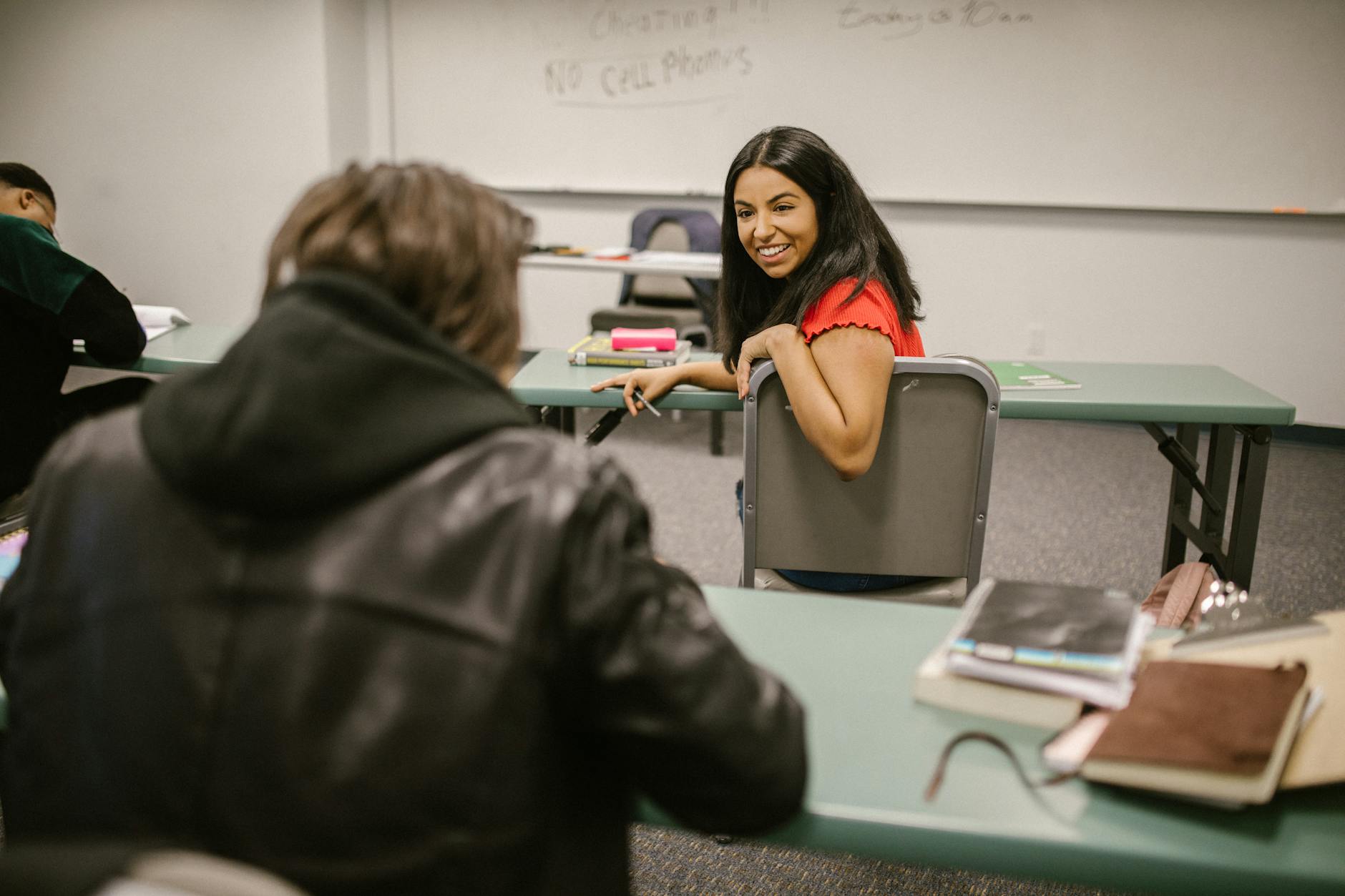 Students chatting during a break in a college classroom, surrounded by study materials and friendly atmosphere.