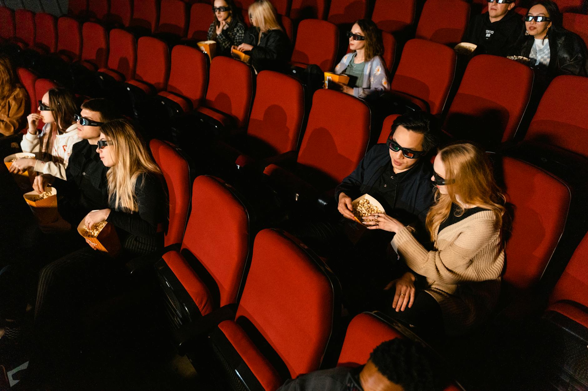 People in a theater wearing 3D glasses watching a movie with popcorn.