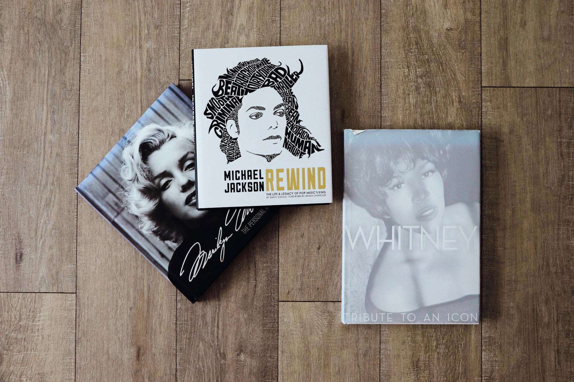 Books featuring Marilyn Monroe, Michael Jackson, and Whitney Houston on a wooden floor.