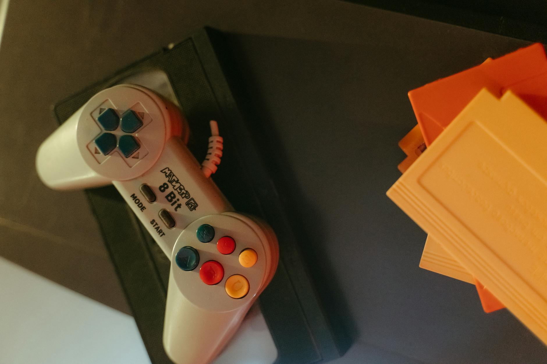 A vintage 8-bit game controller with colorful buttons next to classic game cartridges.
