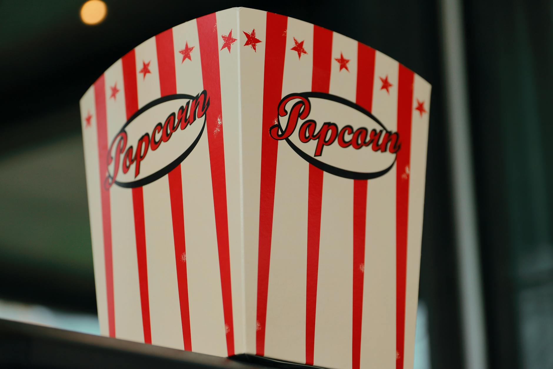 Red and white striped popcorn box indoors, perfect for cinema-themed settings.