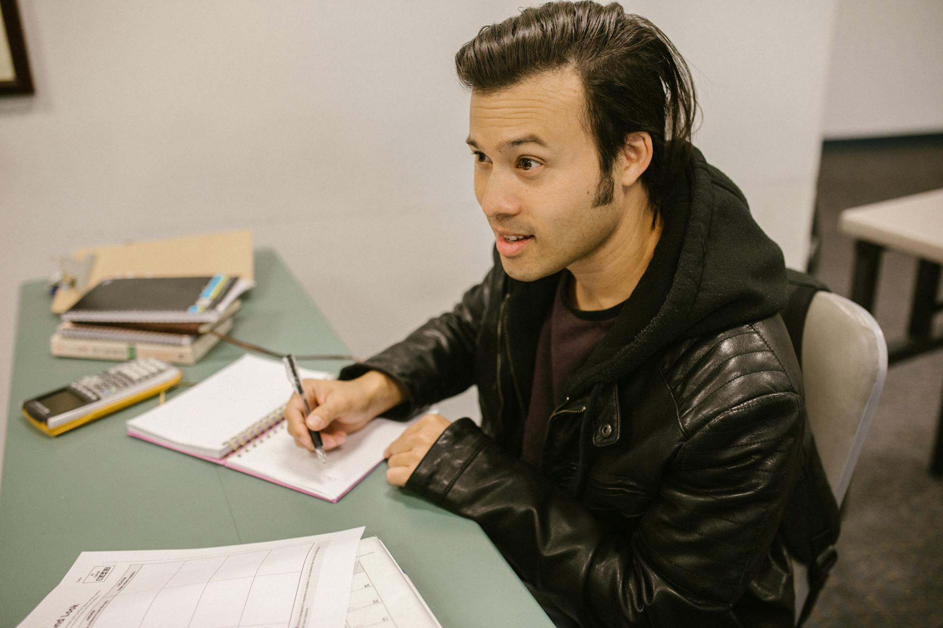 A young man focusing on studying with notebooks, a calculator, and papers on a desk.