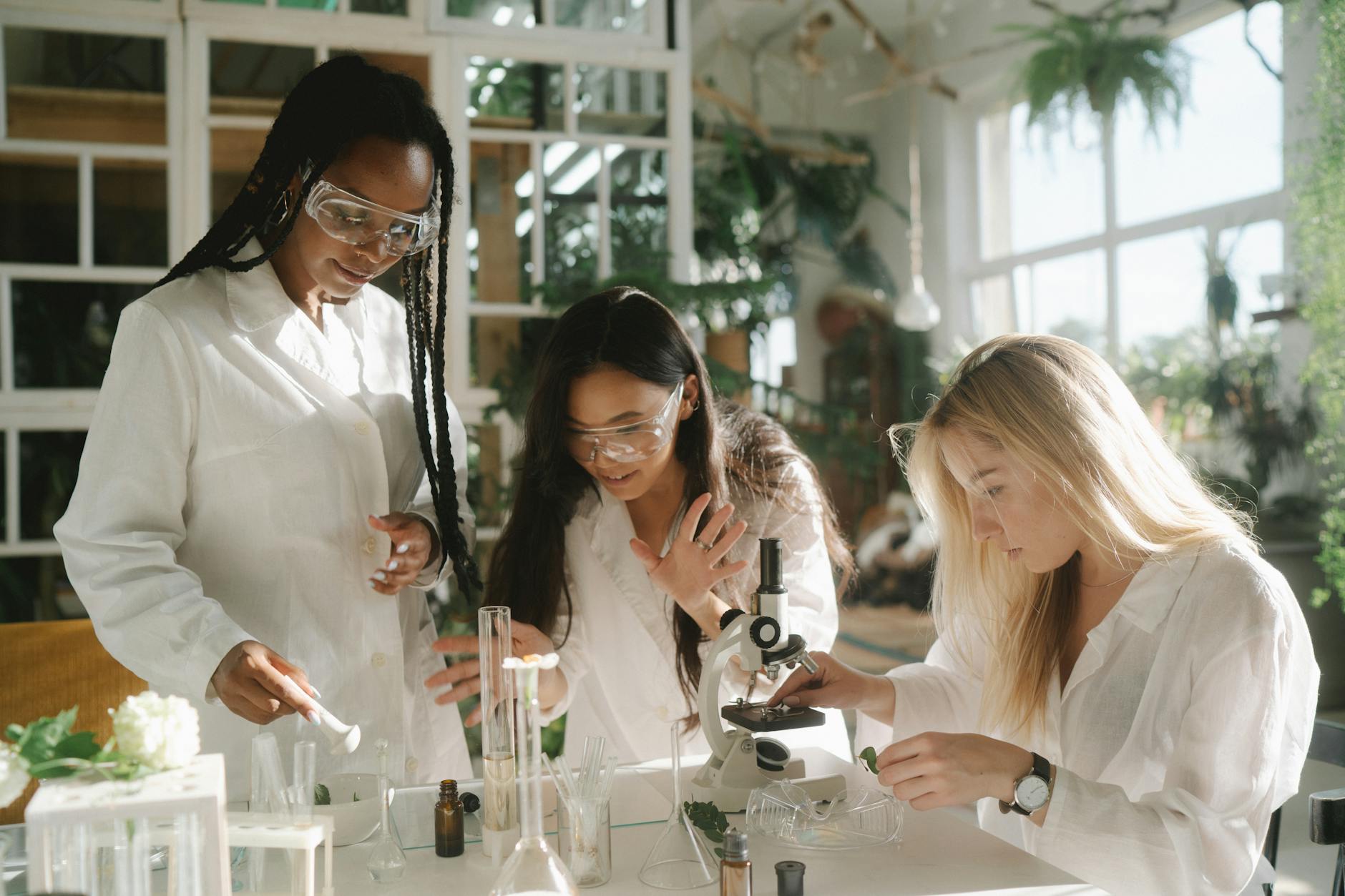 Three multicultural women scientists engage in laboratory experiments with microscopes and glassware.