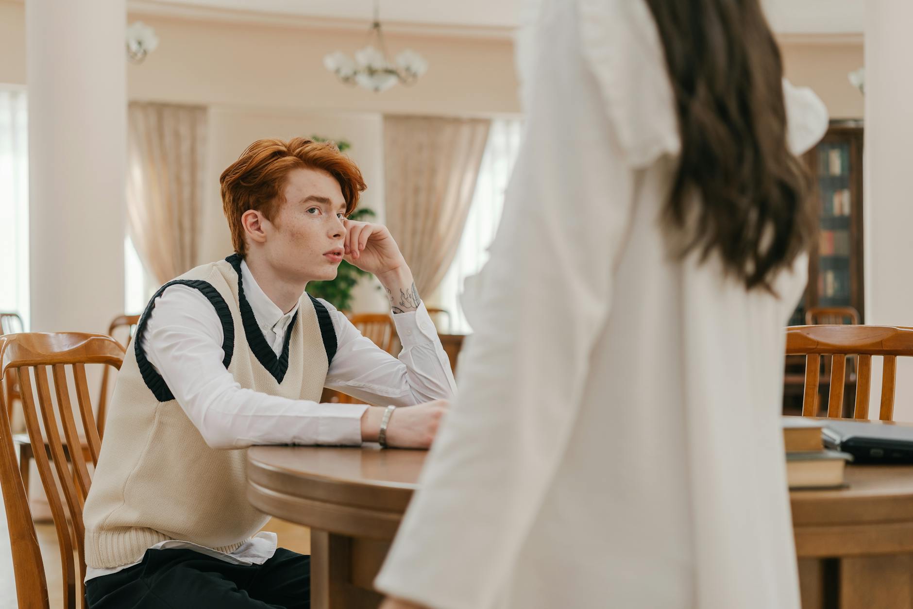 Red-haired student in a library, seated at a table, engaged in a thoughtful discussion.