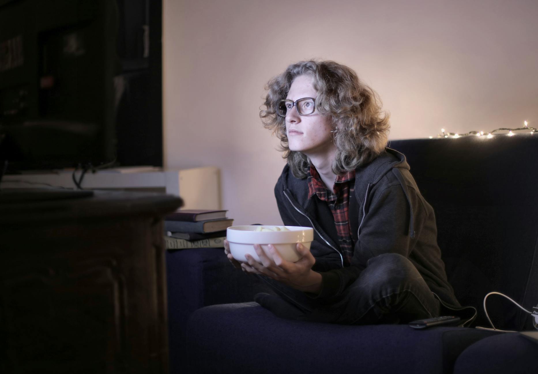 Curly-haired teen enjoys movie night at home with a bowl of popcorn.