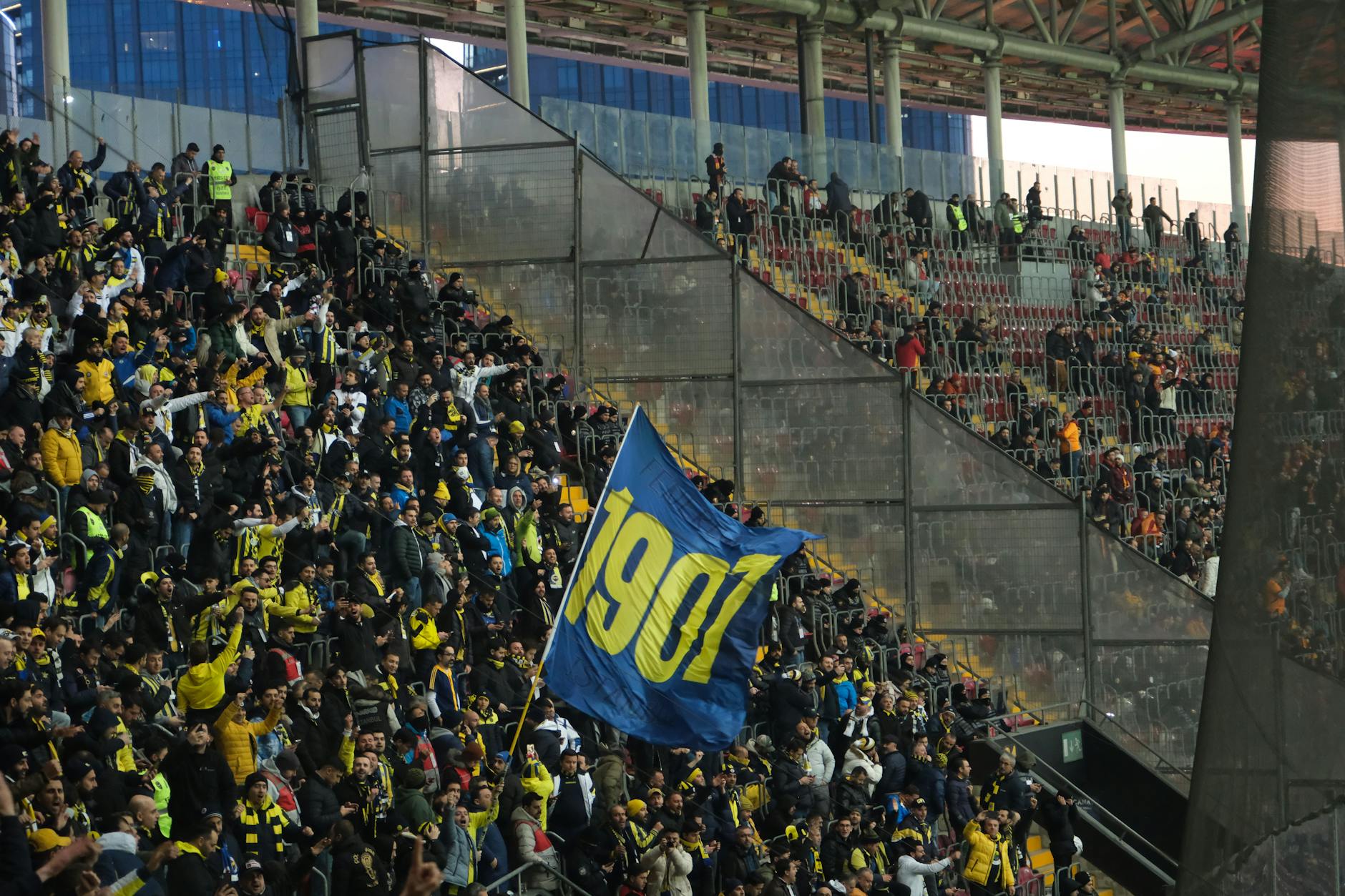 Excited football fans cheering with a prominent flag in a crowded stadium.