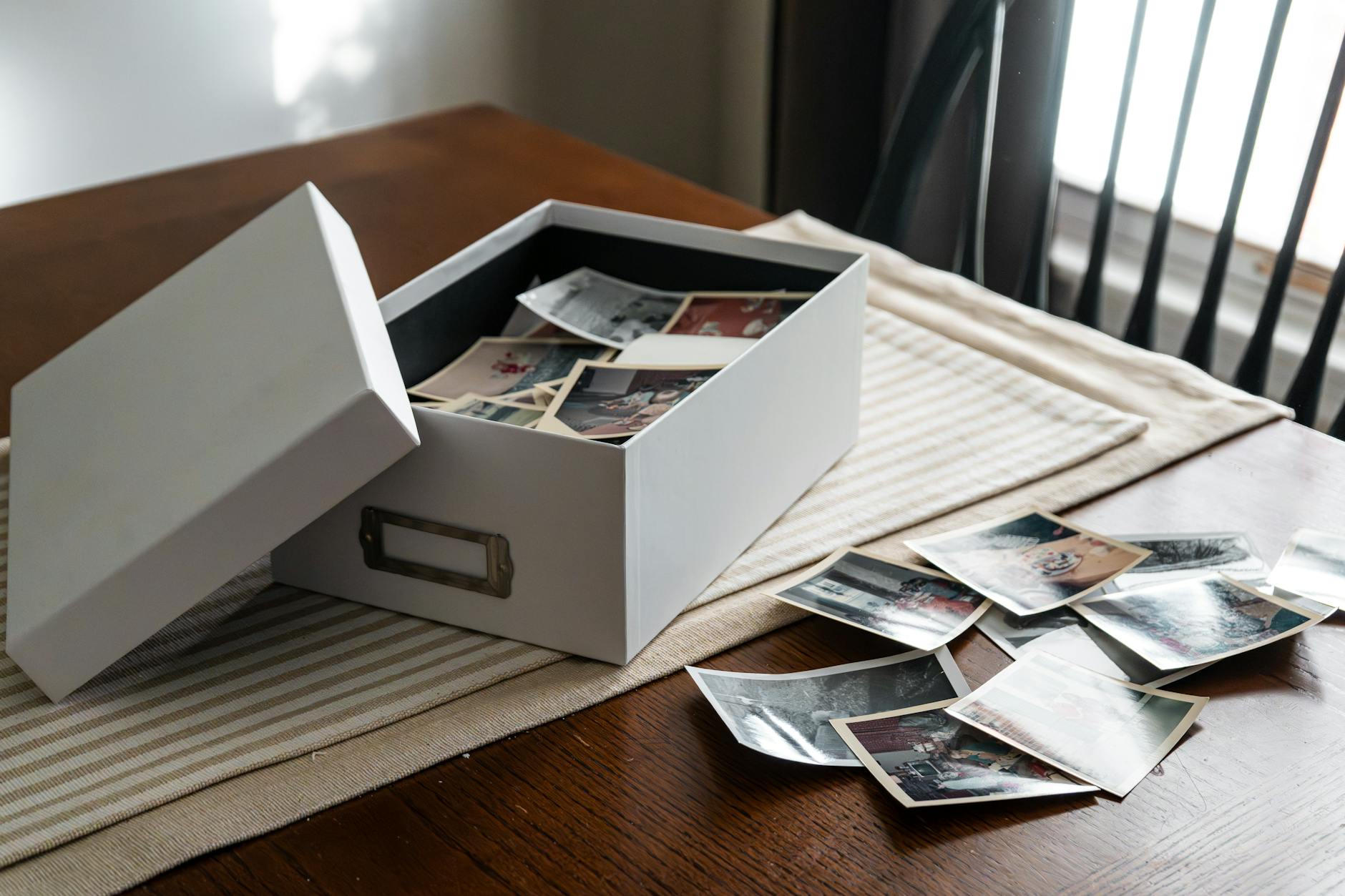 Open box of vintage family photos on wooden table by window.