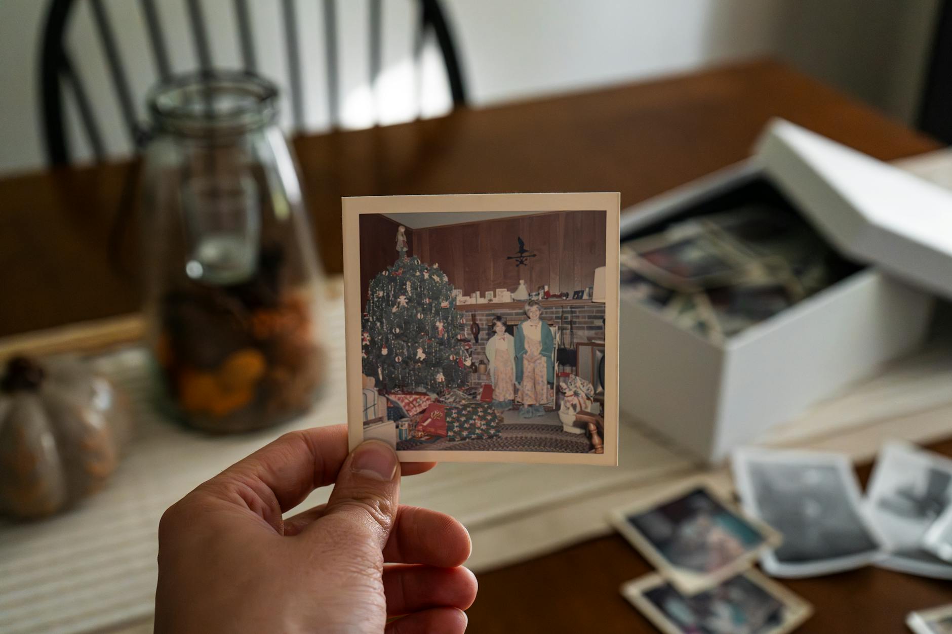 Hand holding an old Christmas photo against a backdrop of family pictures and seasonal decor.