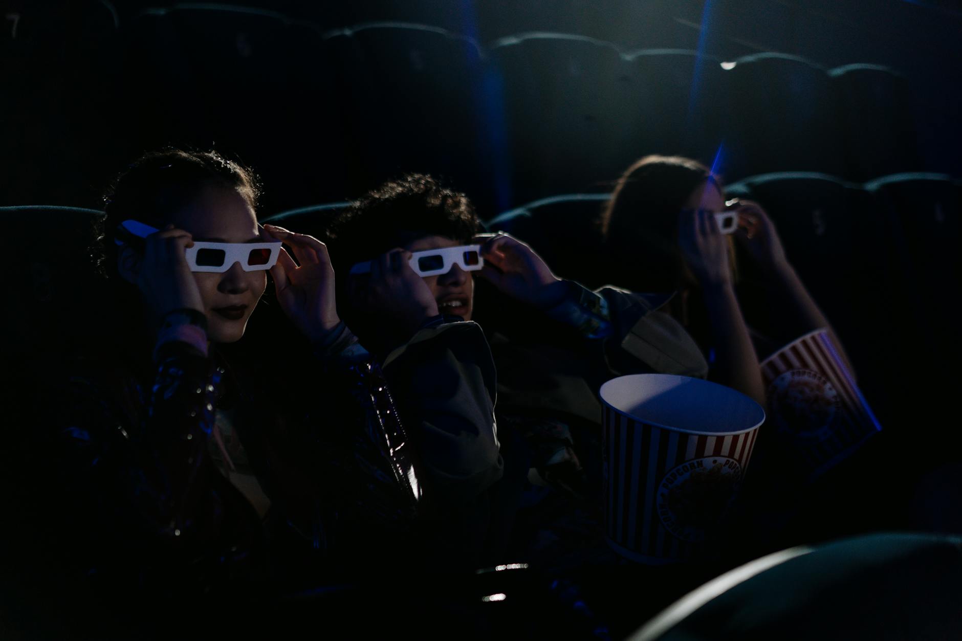 Group of teenagers wearing 3D glasses in a cinema with popcorn during a movie.