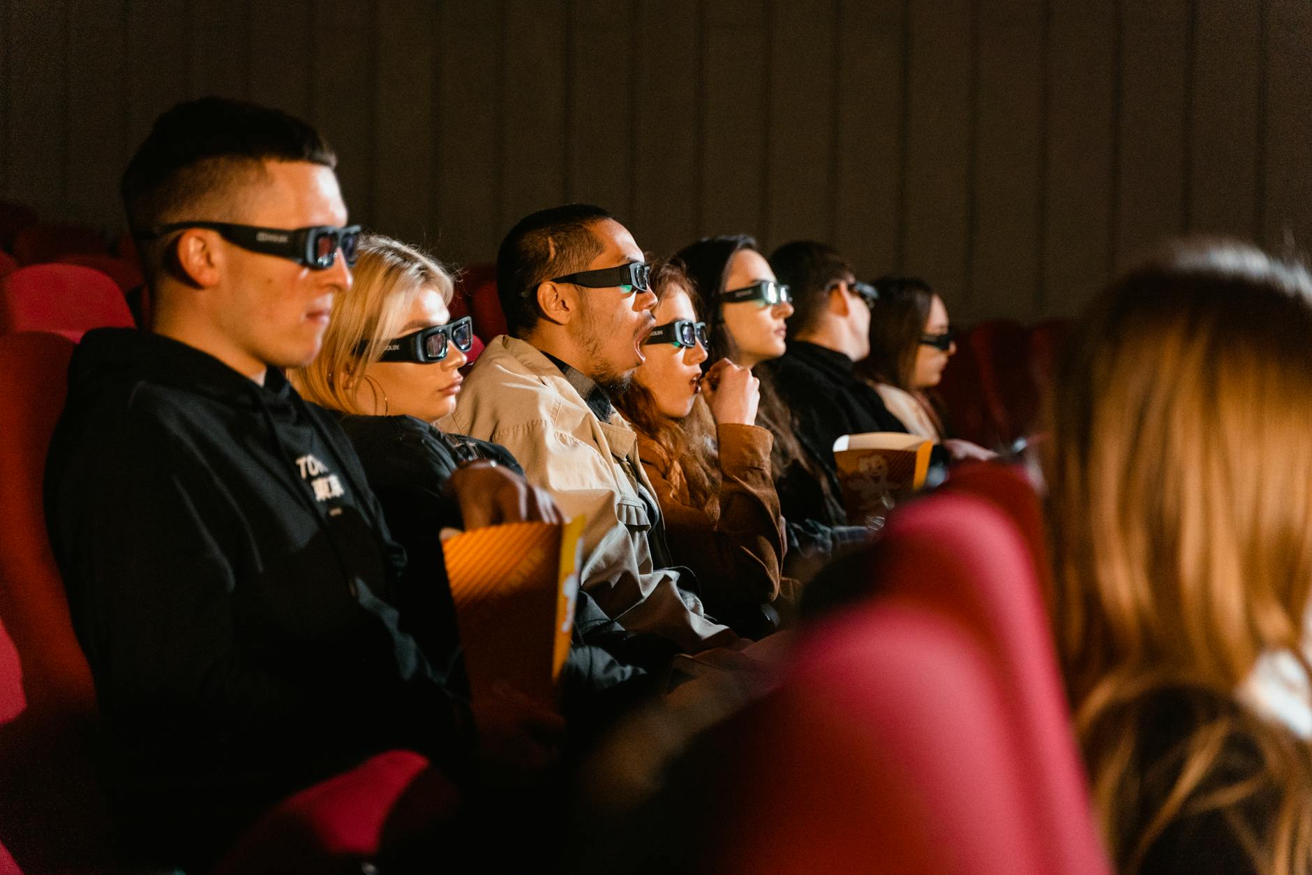 Audience wearing 3D glasses enjoying a movie in a cinema with popcorn.
