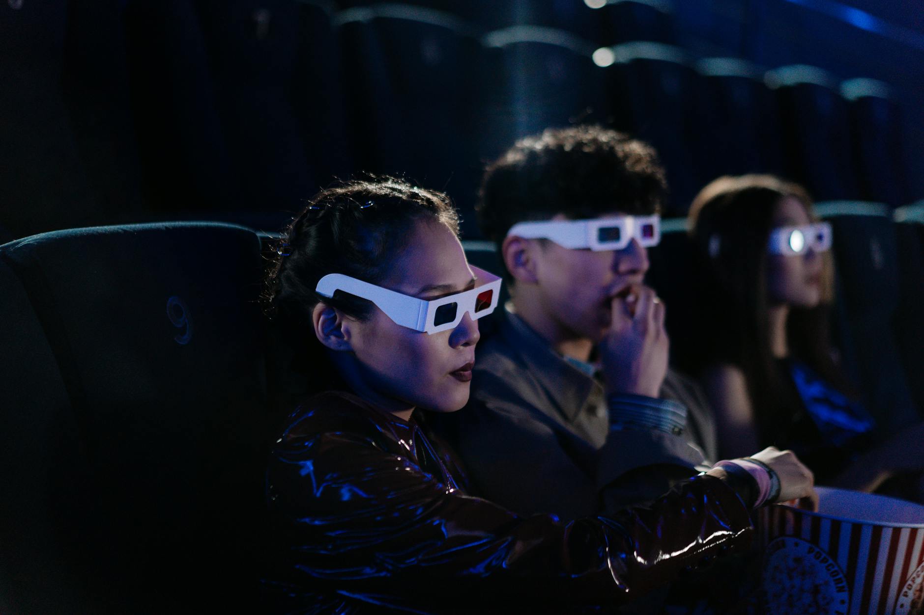 Friends enjoying a 3D movie night at the cinema, wearing glasses and eating popcorn.