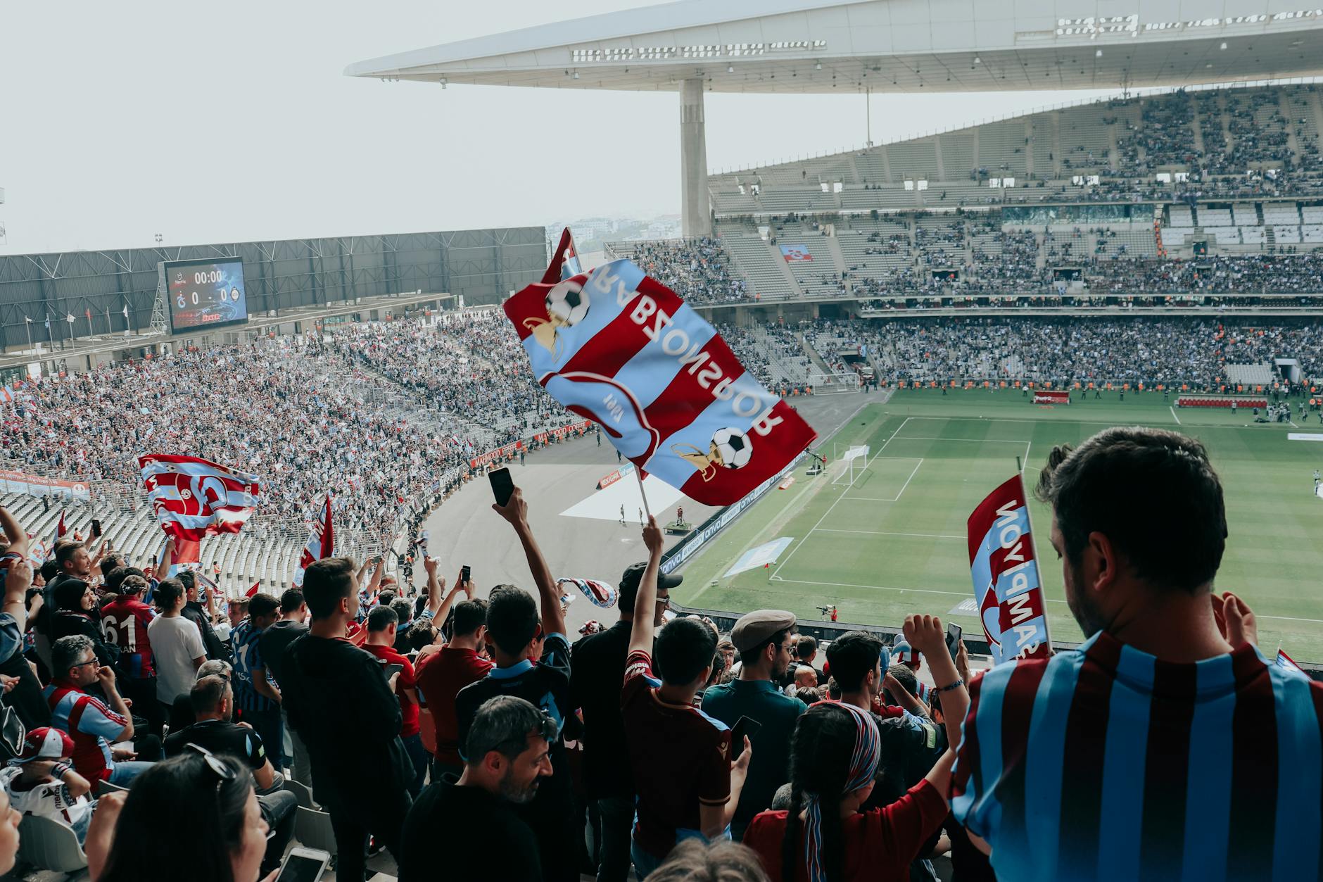 Vibrant crowd cheers at a football match in a large stadium, waving team flags.
