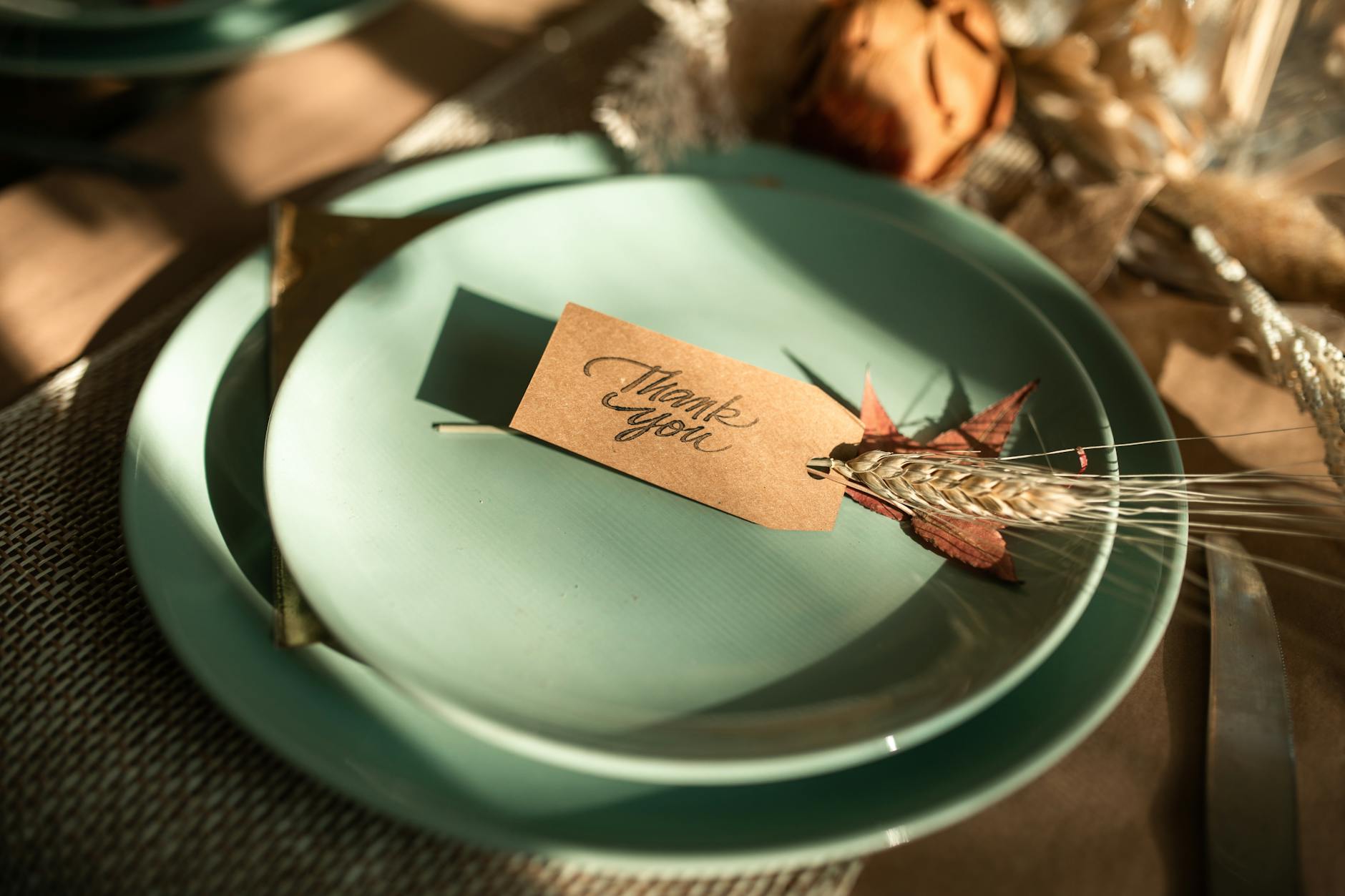 A sophisticated Thanksgiving table setup featuring a 'Thank You' card on mellow green plates, perfect for seasonal celebrations.