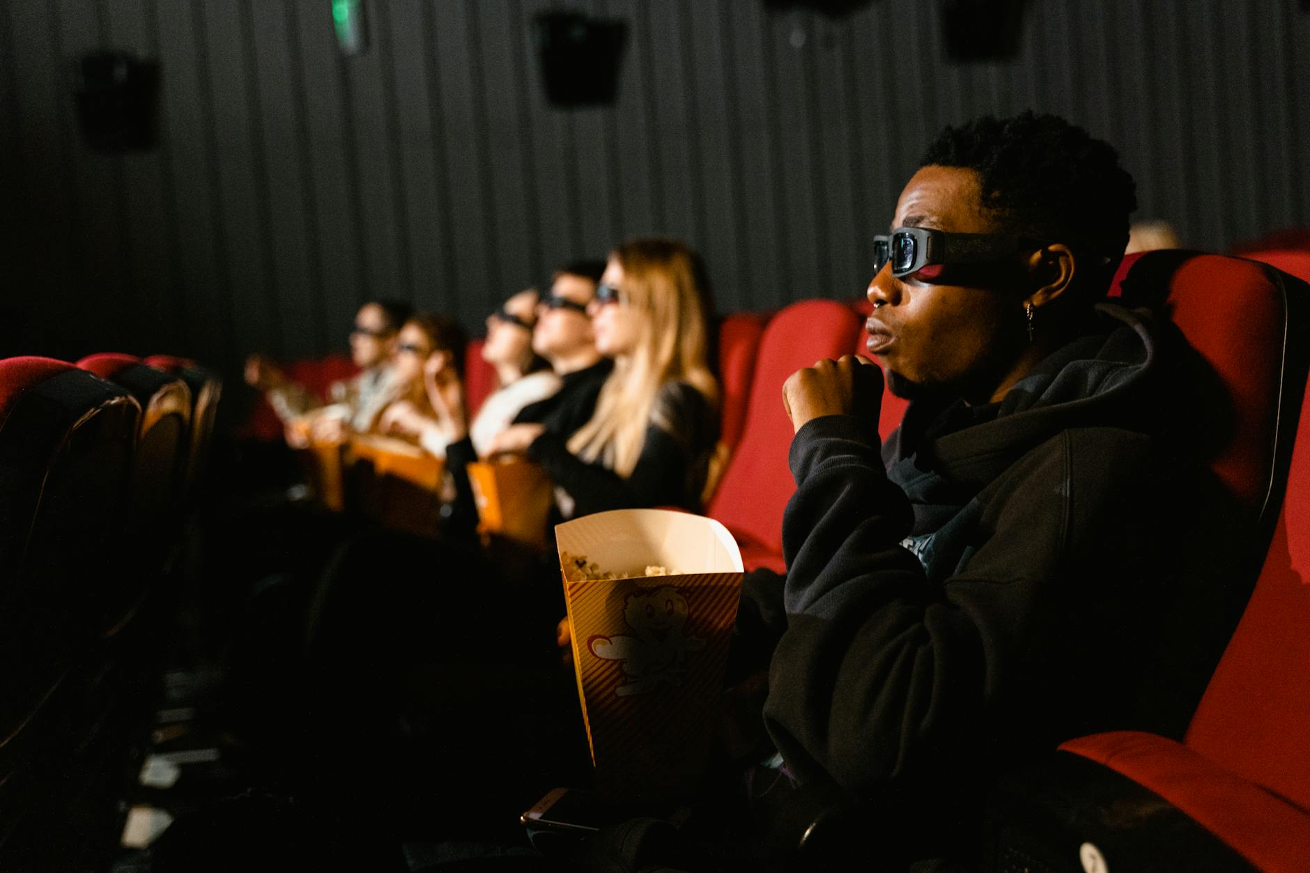 A group of diverse adults wearing 3D glasses enjoying a movie indoors.