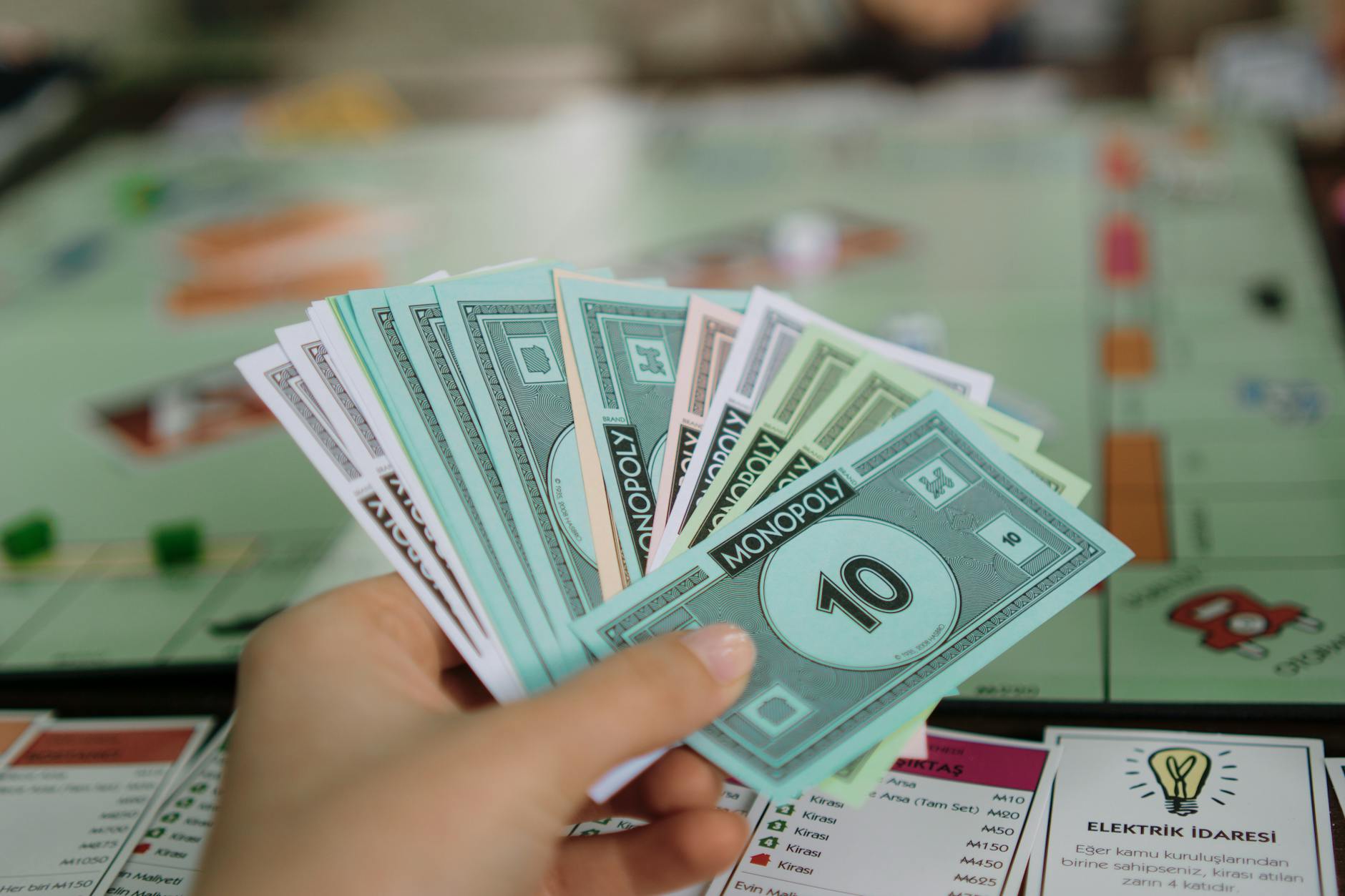 Close-up of a hand holding Monopoly money with board game in the background.