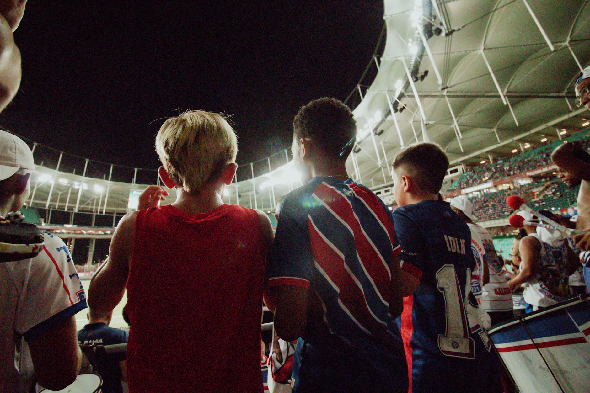 Fans cheer from the stands during a night soccer game in a large stadium, full of energy and excitement.