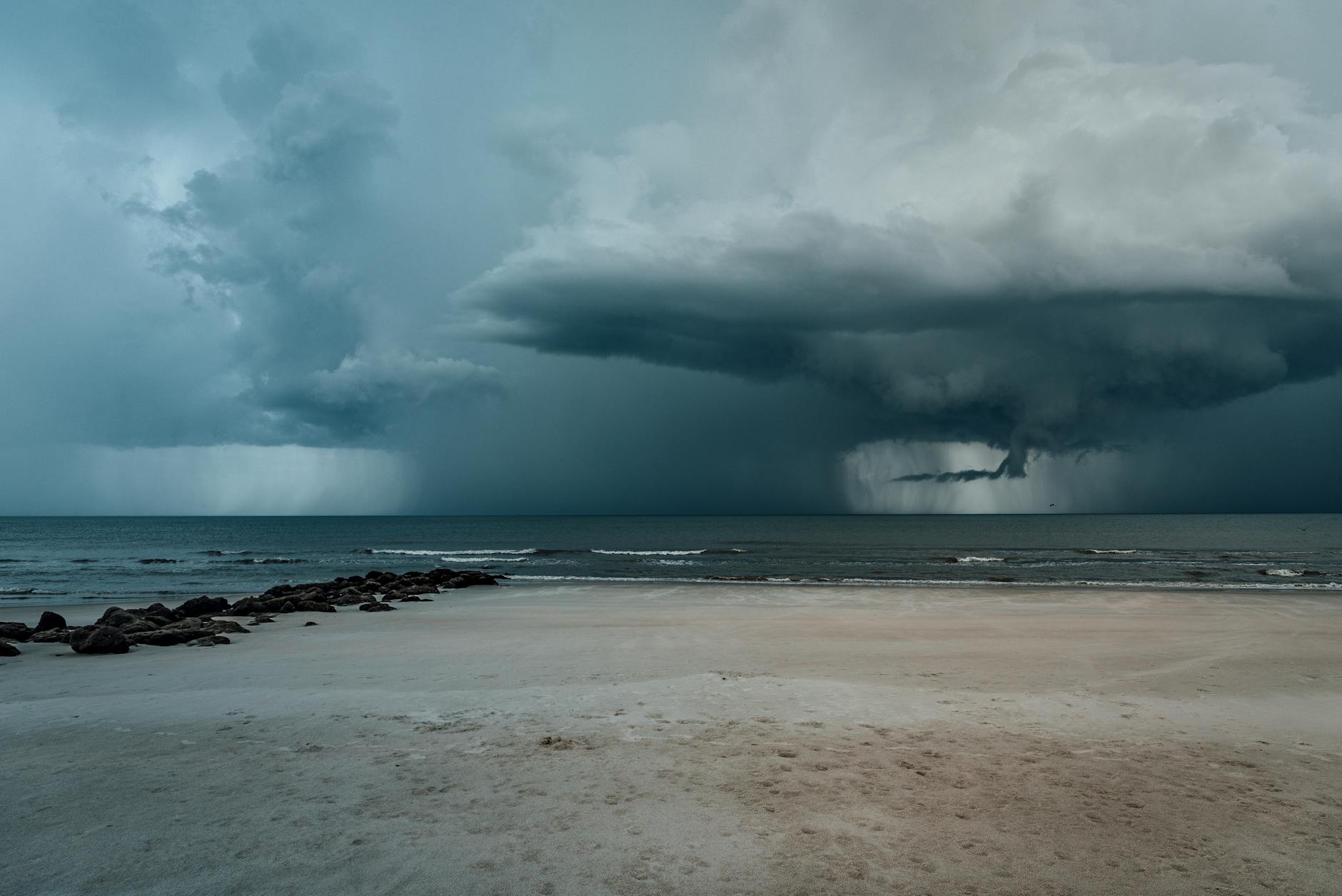 A powerful storm approaches a serene sandy beach with dramatic clouds and turbulent waves.