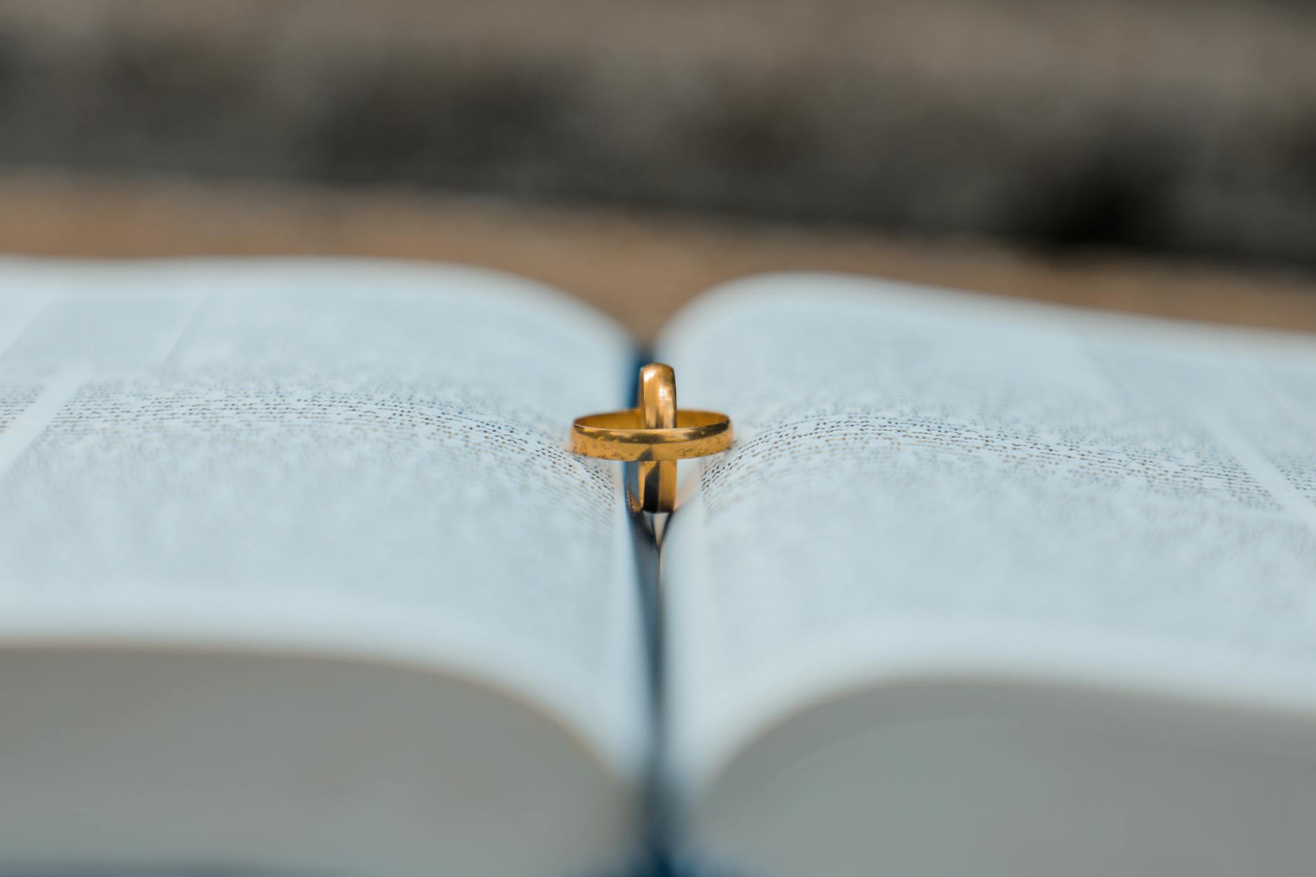A close-up of a gold wedding ring placed on an open book, symbolizing union and tradition.